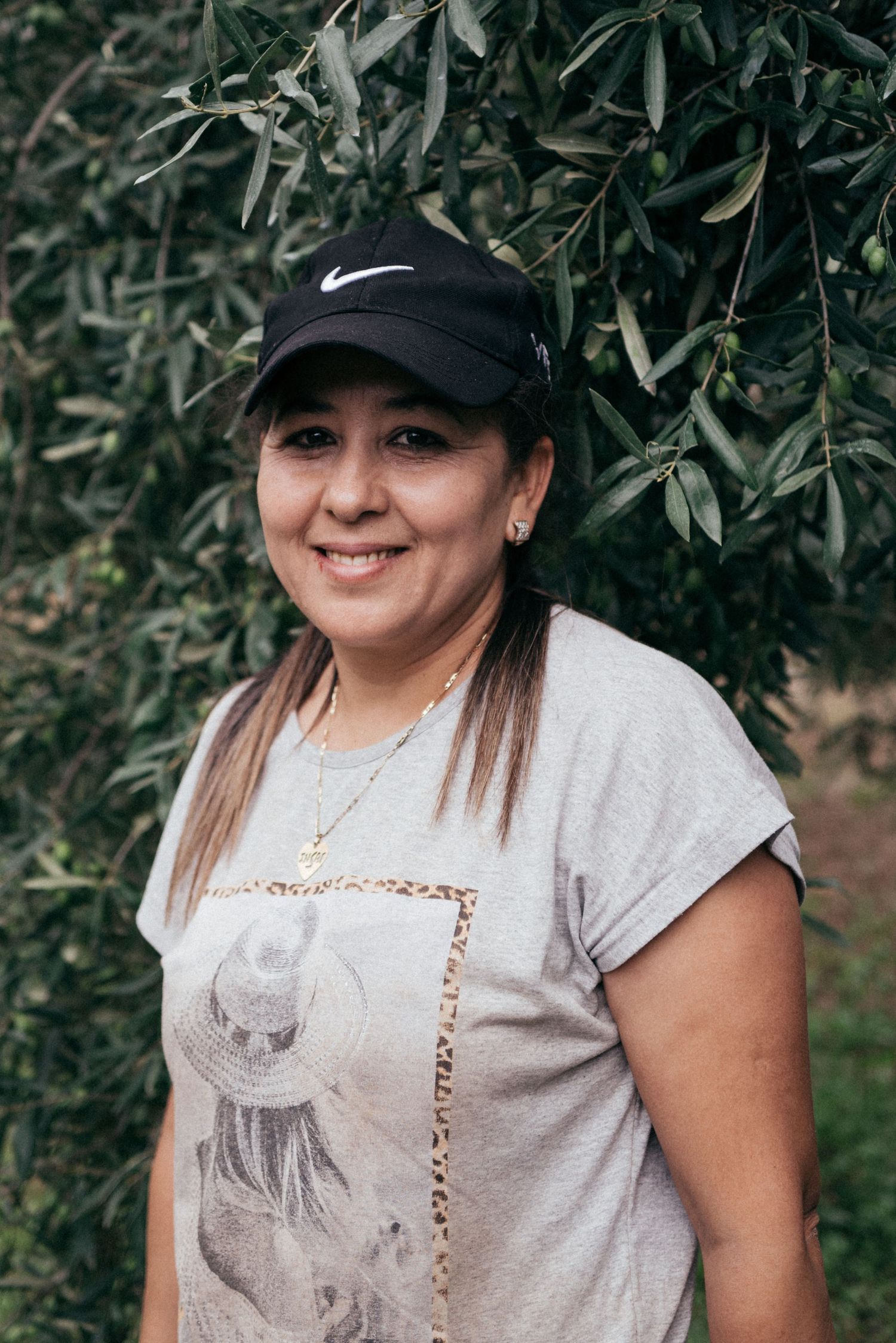 Someone wearing a Nike cap and gray t-shirt poses against green foliage in an outdoor setting.