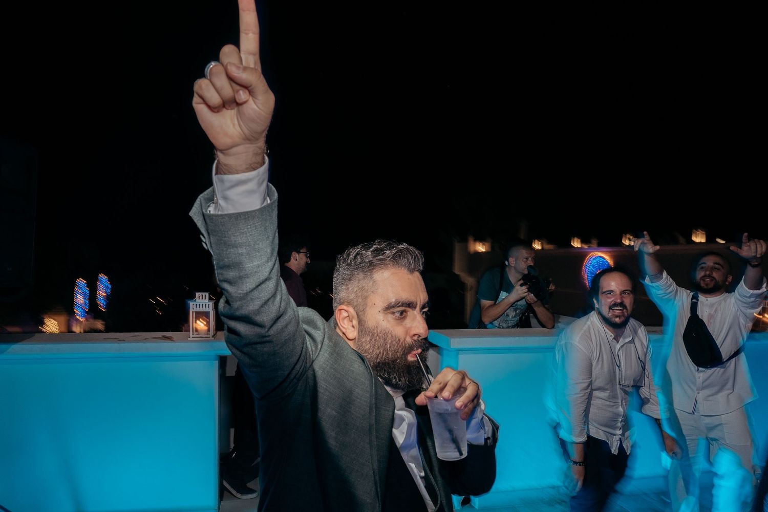 Guest celebrating with raised hand at outdoor nighttime wedding reception.