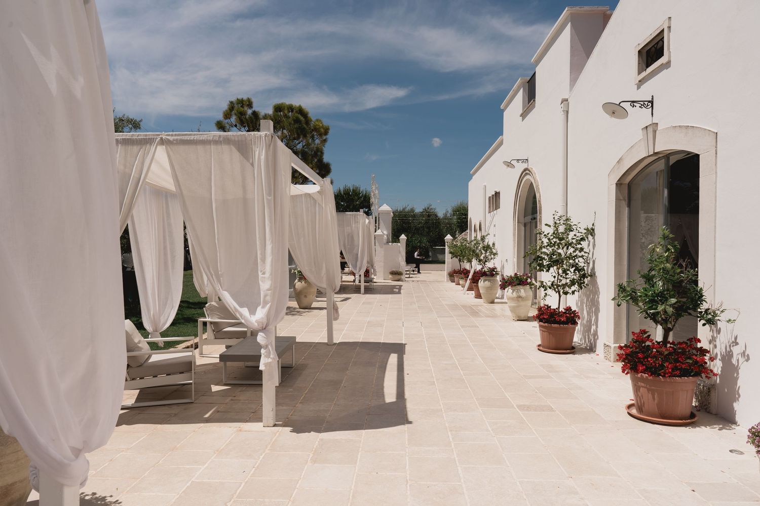 White Mediterranean courtyard with flowing curtains and terracotta planters along pathway.