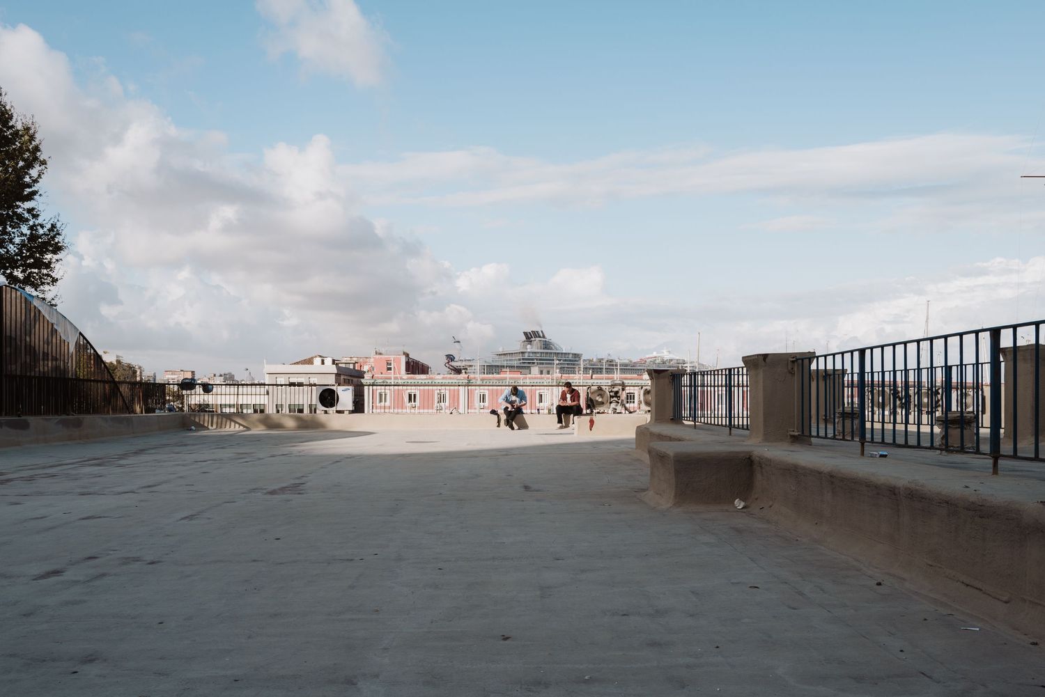 A wide open concrete terrace overlooking coastal buildings under a bright blue sky.