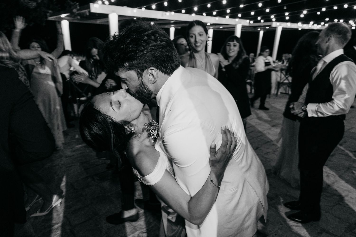 A romantic couple sharing an intimate dance under twinkling string lights at an evening reception.
