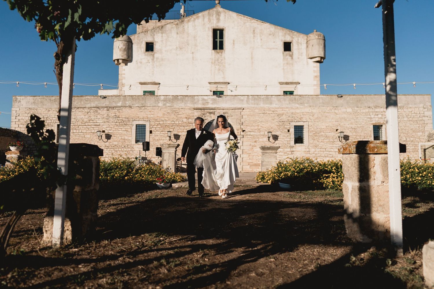 A wedding party poses in front of a historic white church building in Mediterranean style.