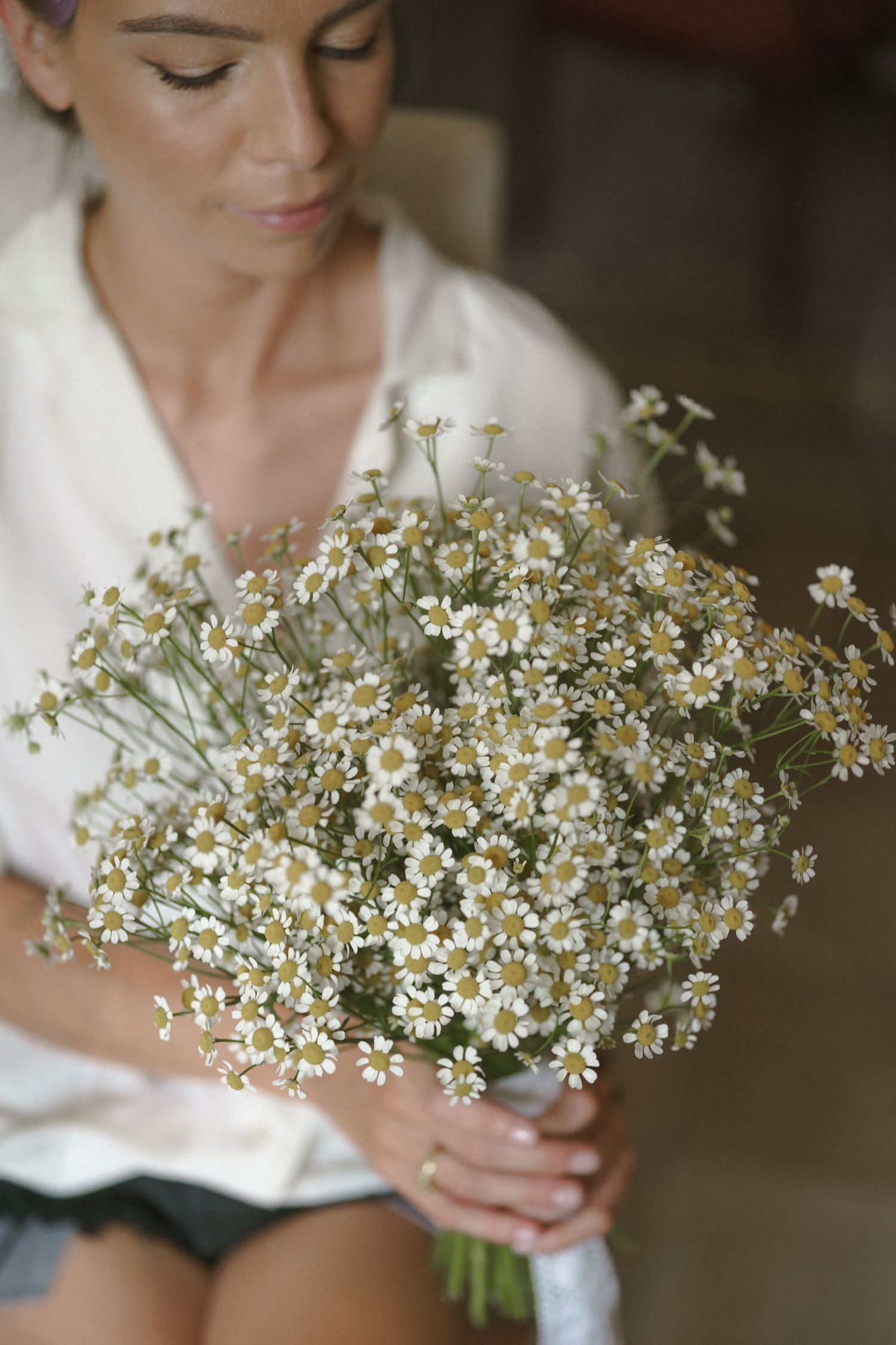 A delicate bouquet of white wildflowers and baby's breath held by someone wearing a white dress.