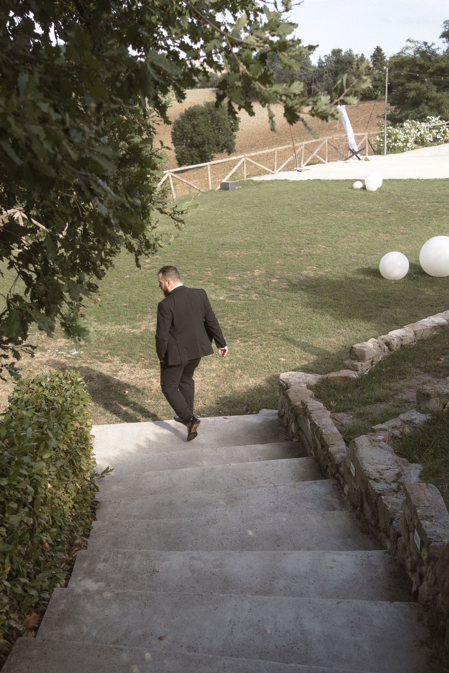 Person walking down concrete steps with white decorative balloons and trees along the pathway.