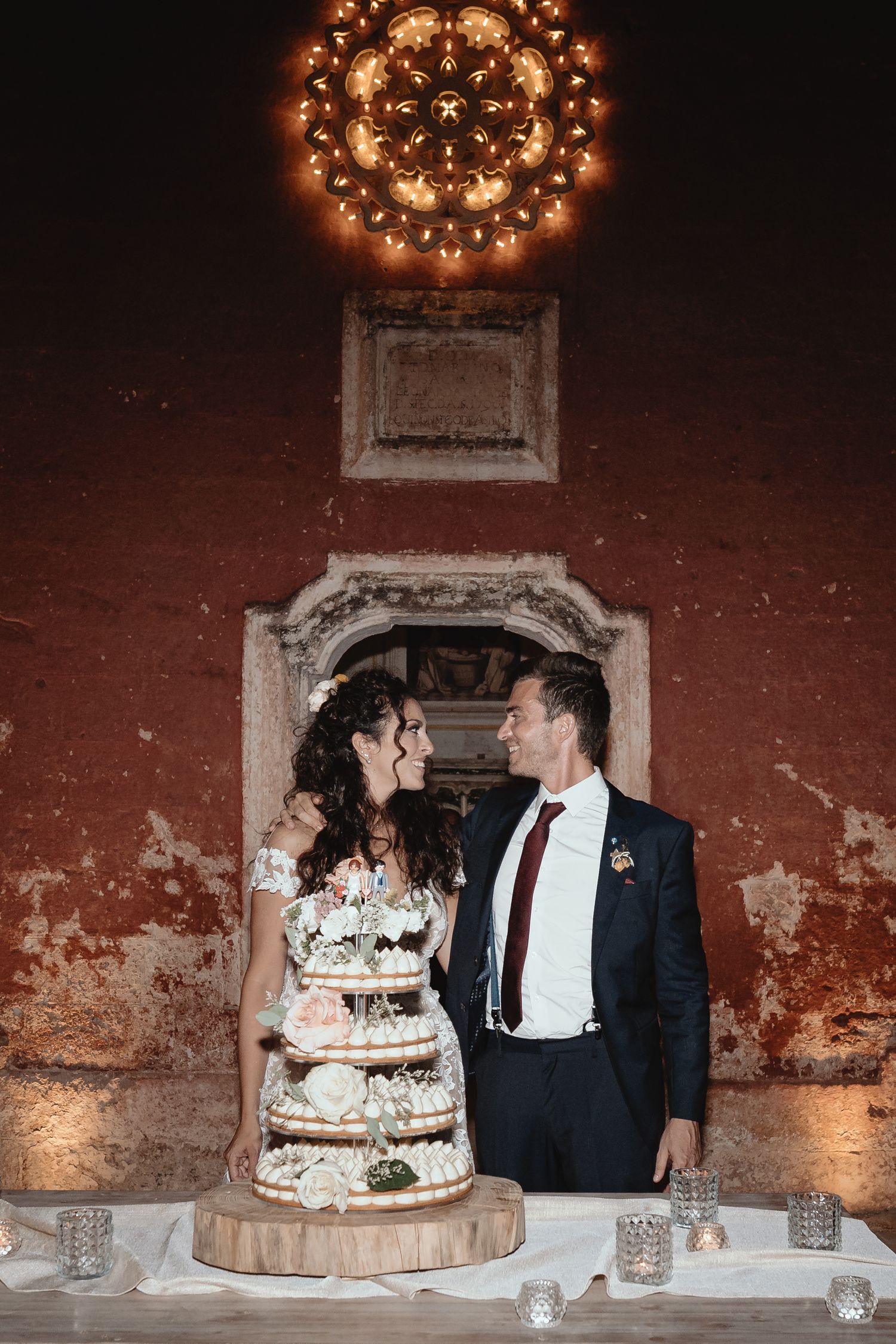 Wedding cake cutting scene with rustic brick wall backdrop and twinkling lights overhead.