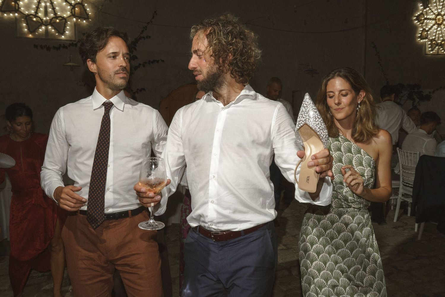 Wedding guests in white shirts socializing and holding drinks during reception celebration.
