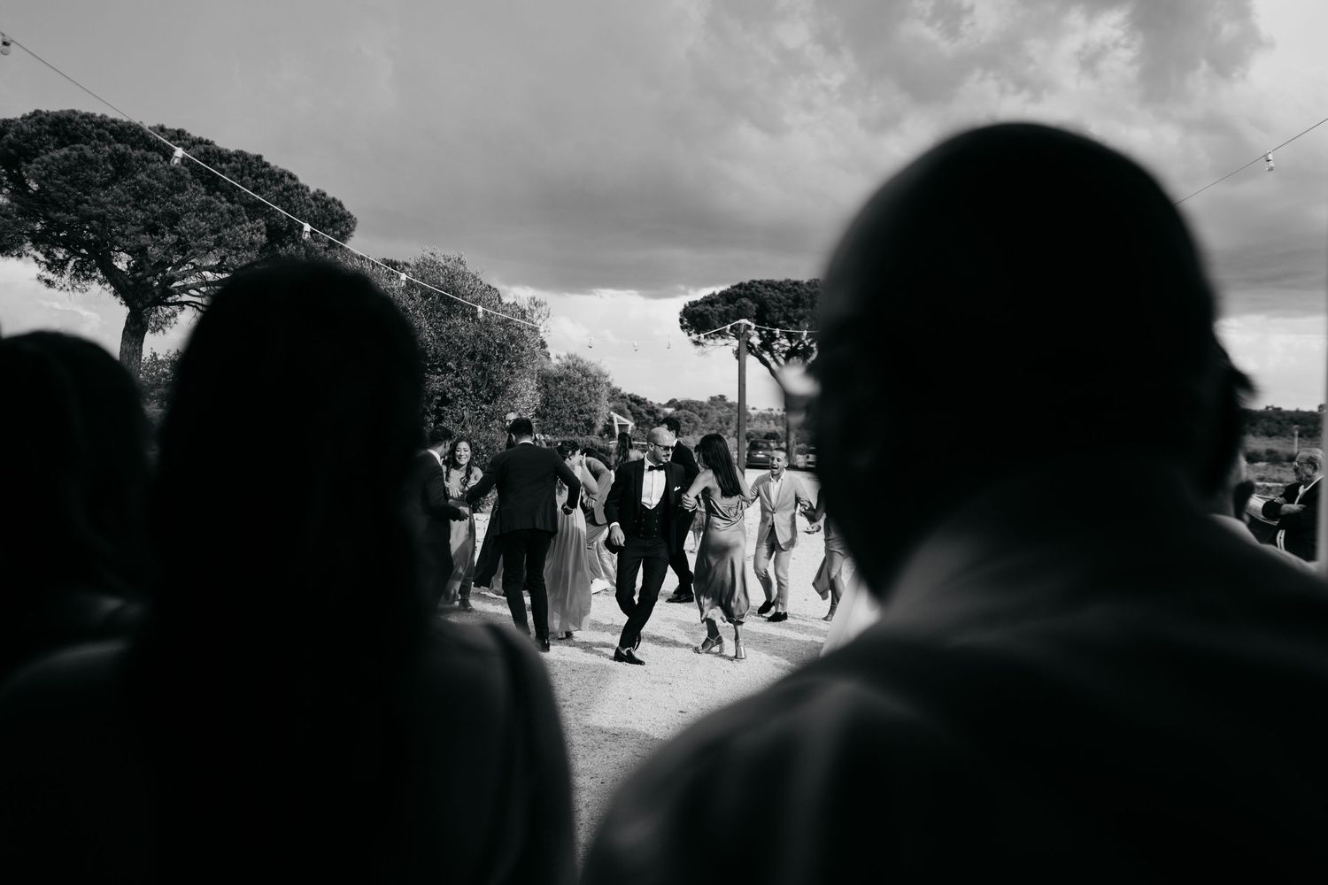 Black and white silhouette of wedding guests against cloudy sky.