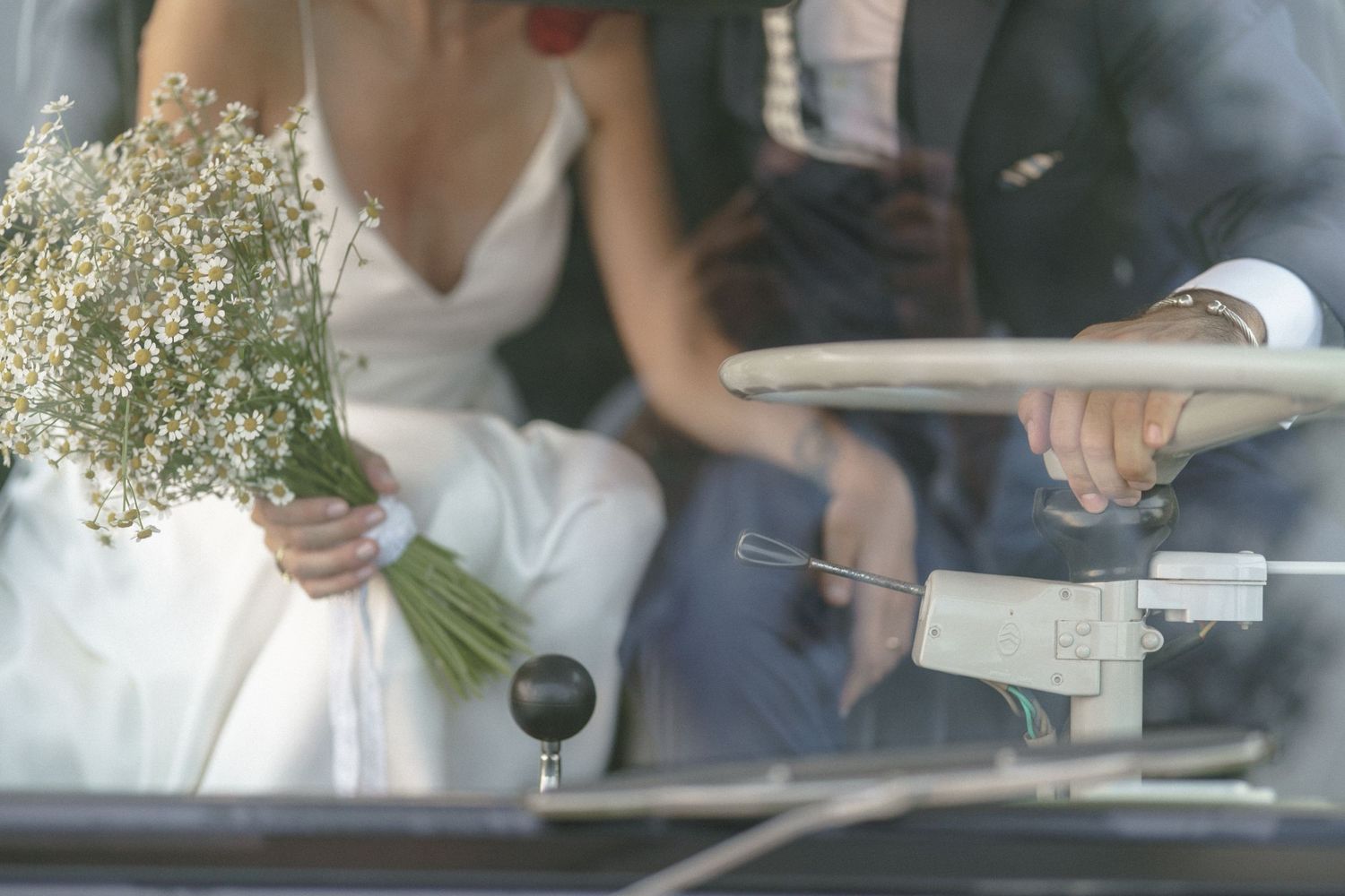 Wedding scene with bride holding baby's breath bouquet and sitting at table with place settings.