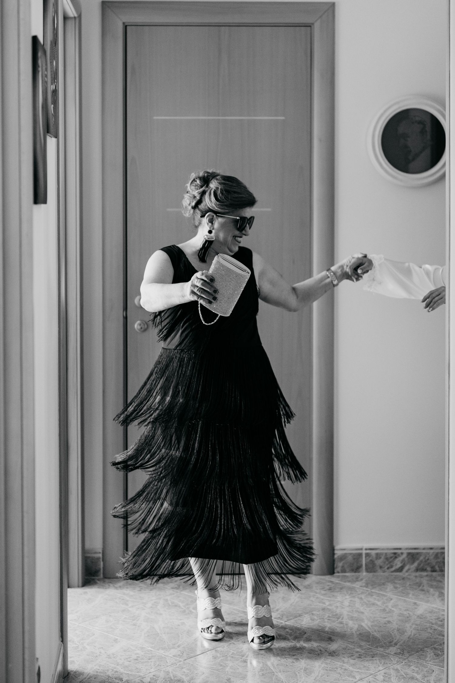 Woman in black fringe dress and sunglasses holding clutch, black and white photo.
