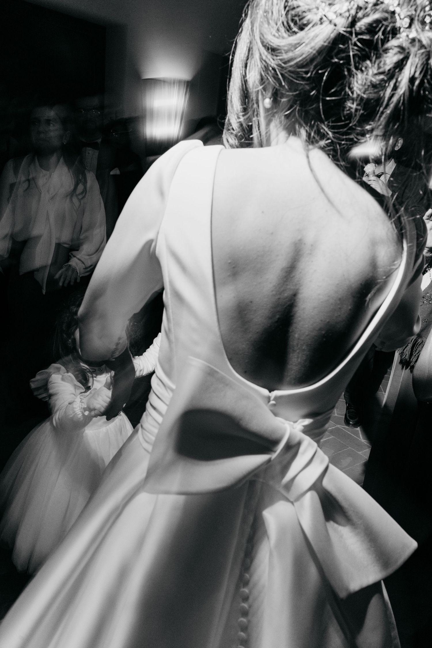 Black and white back view of bride in elegant open-back wedding gown with bow detail dancing.