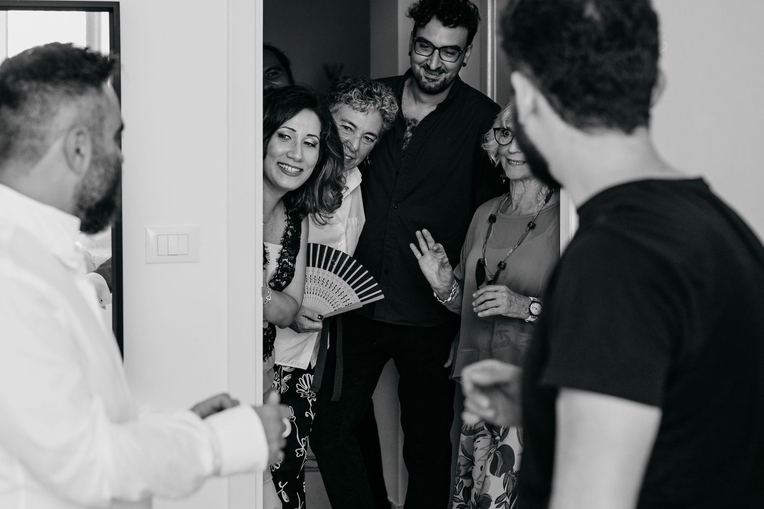 A group of people laughing together in a candid black and white moment during a wedding preparation.