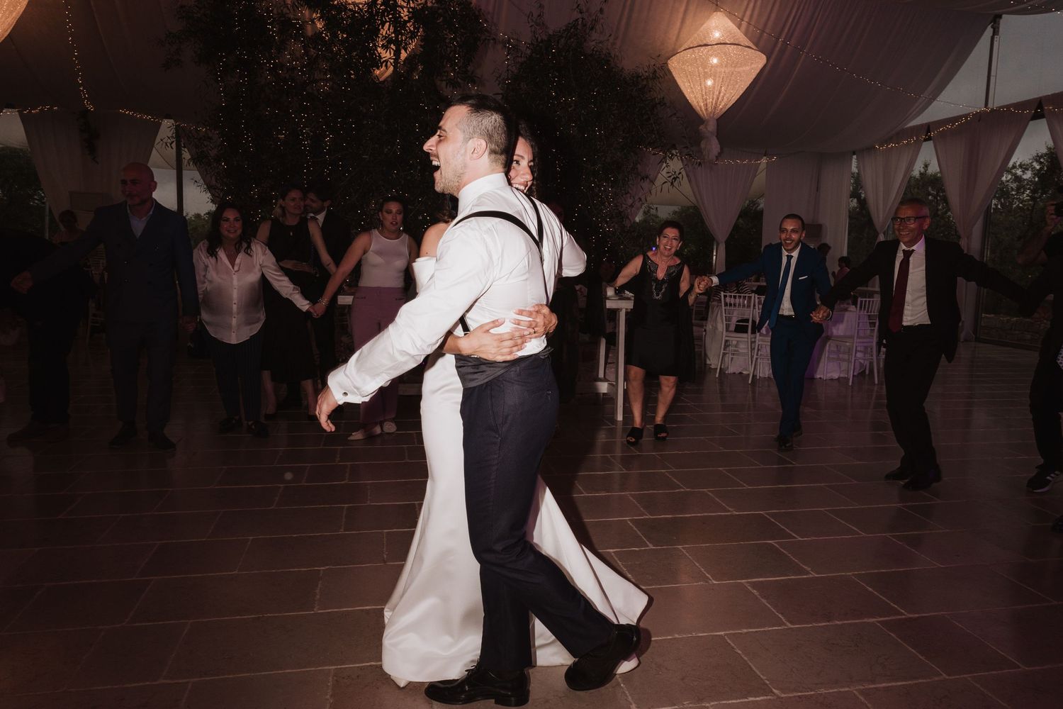 Couples dancing at an elegantly decorated wedding reception under draped fabric and lights.