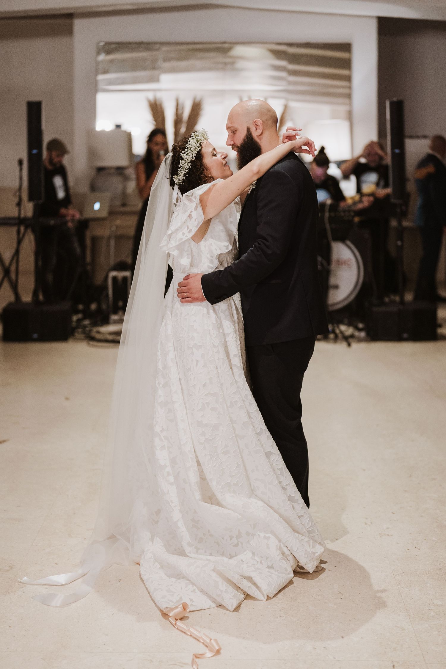 A romantic first dance moment during an indoor wedding reception with a band in the background.