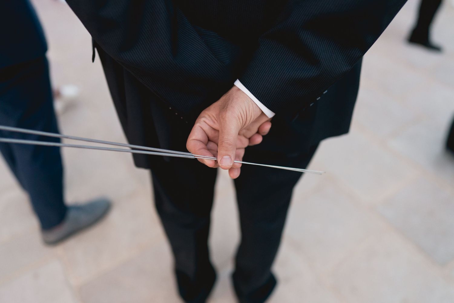 Close-up shot of hands in formal attire holding a thin string or wire.