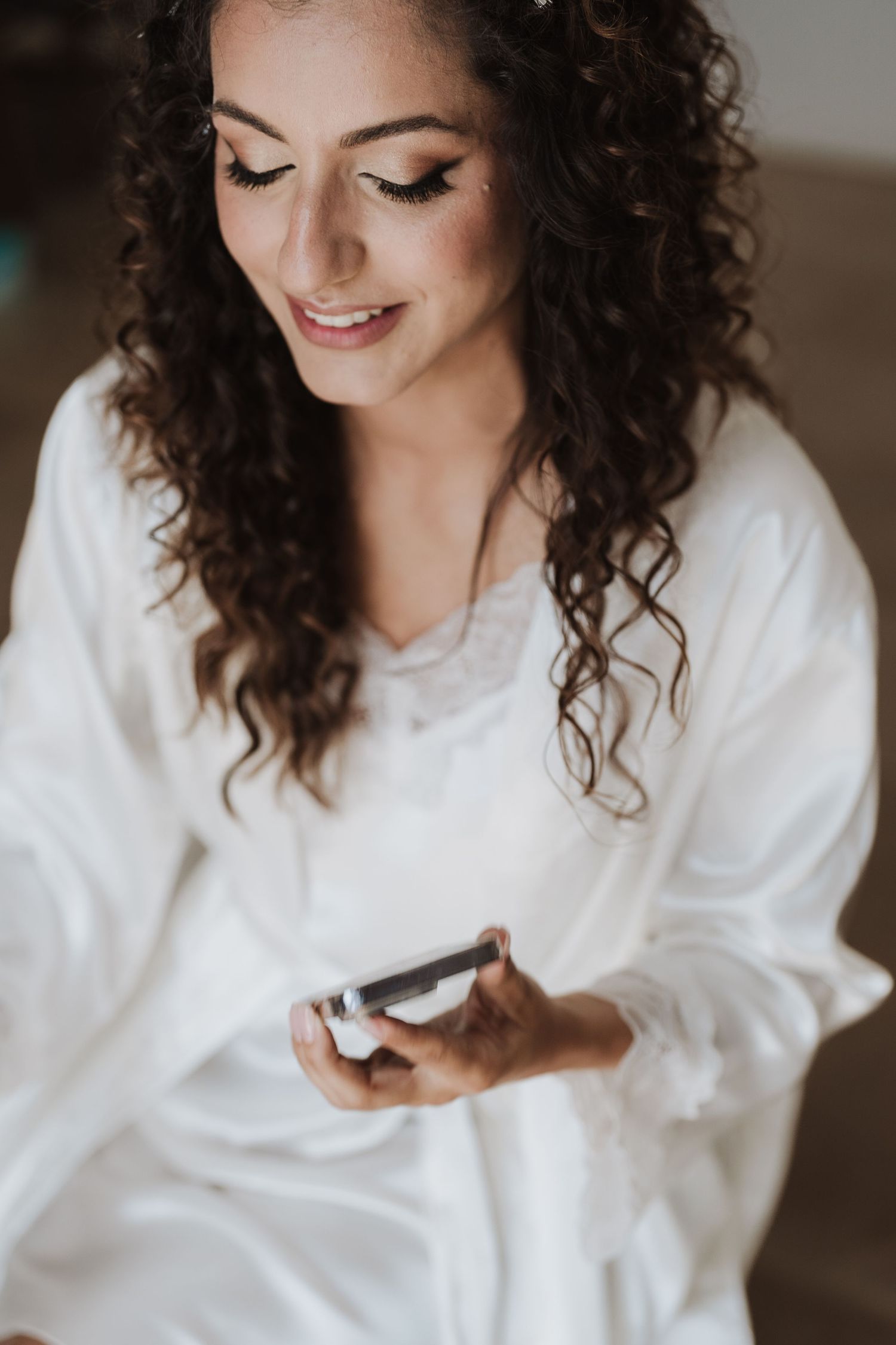 Woman with curly hair in white sweater looking down while holding something.