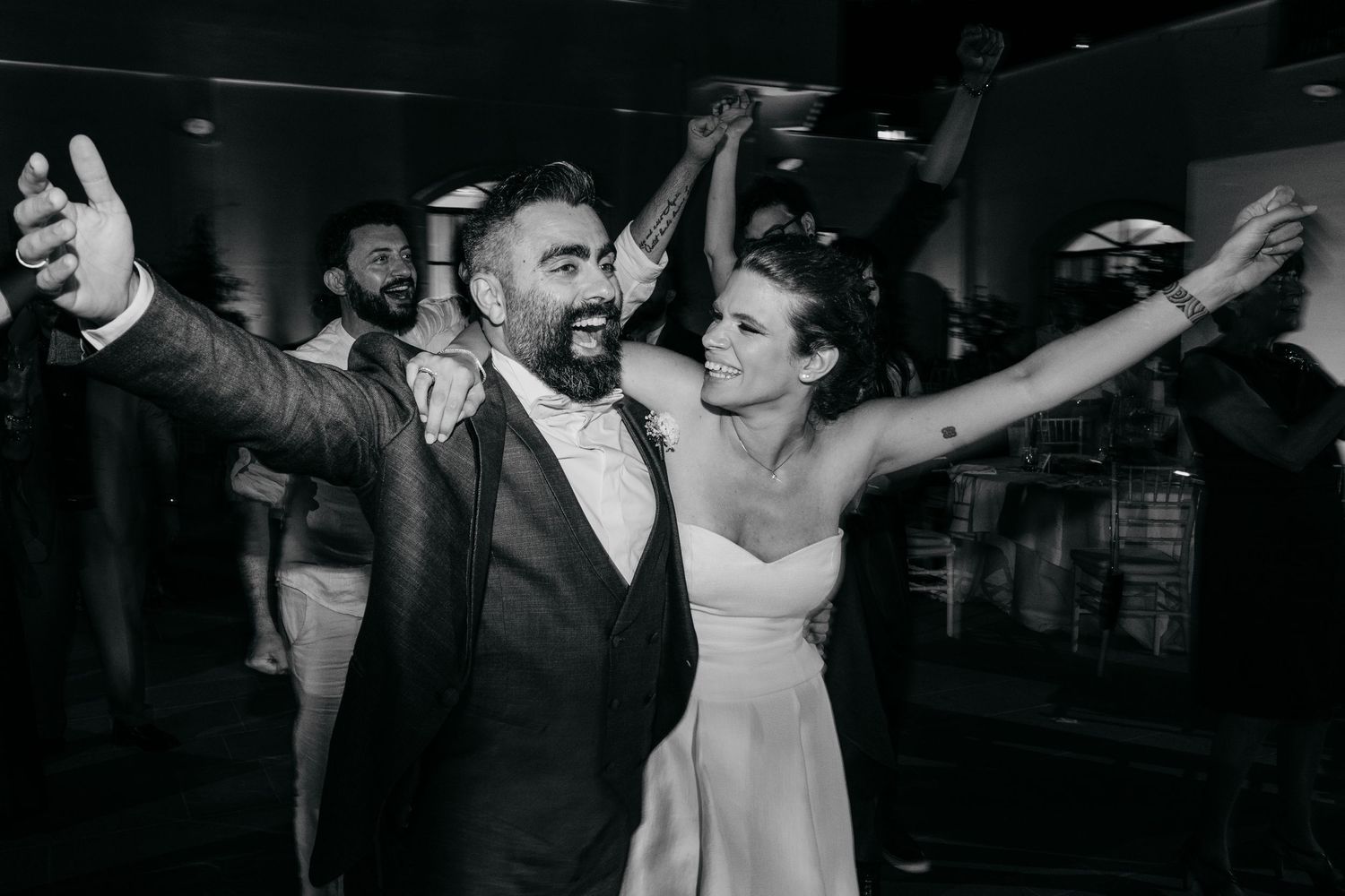 Black and white image shows celebratory dancing moments at an elegant indoor reception.