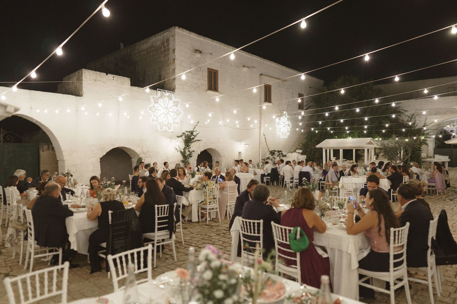 Evening wedding reception in elegant white venue with string lights and decorated dining tables.