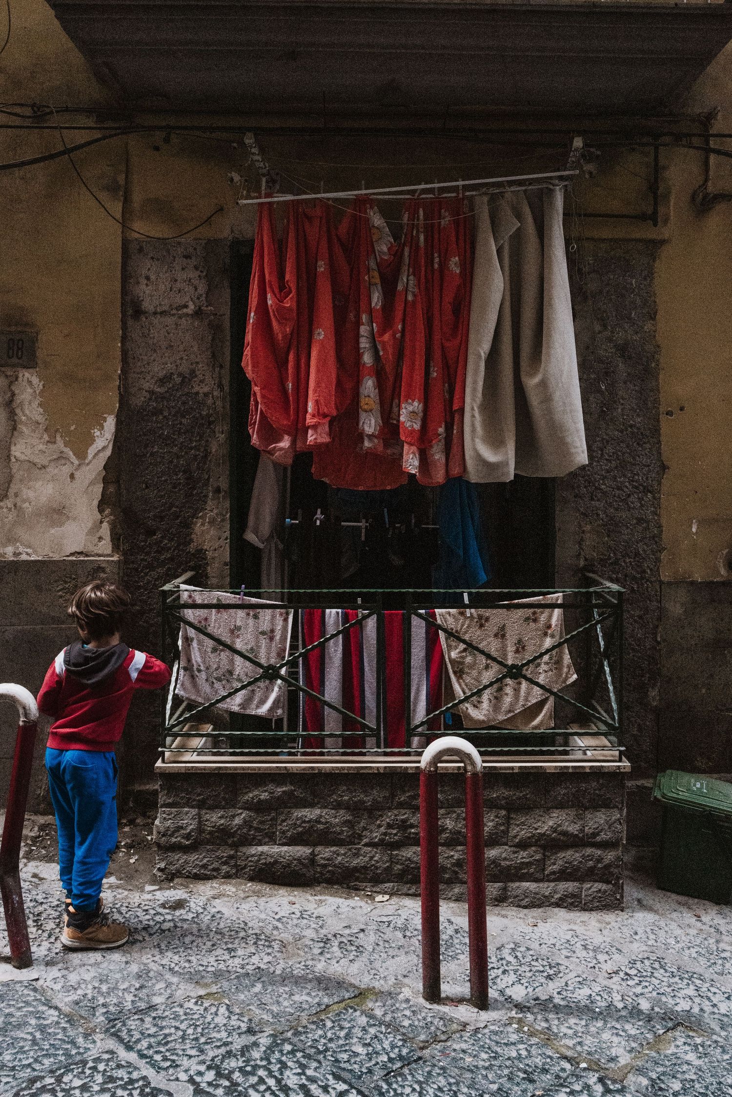 Red and white laundry hangs from a rustic balcony railing in an old Italian neighborhood.