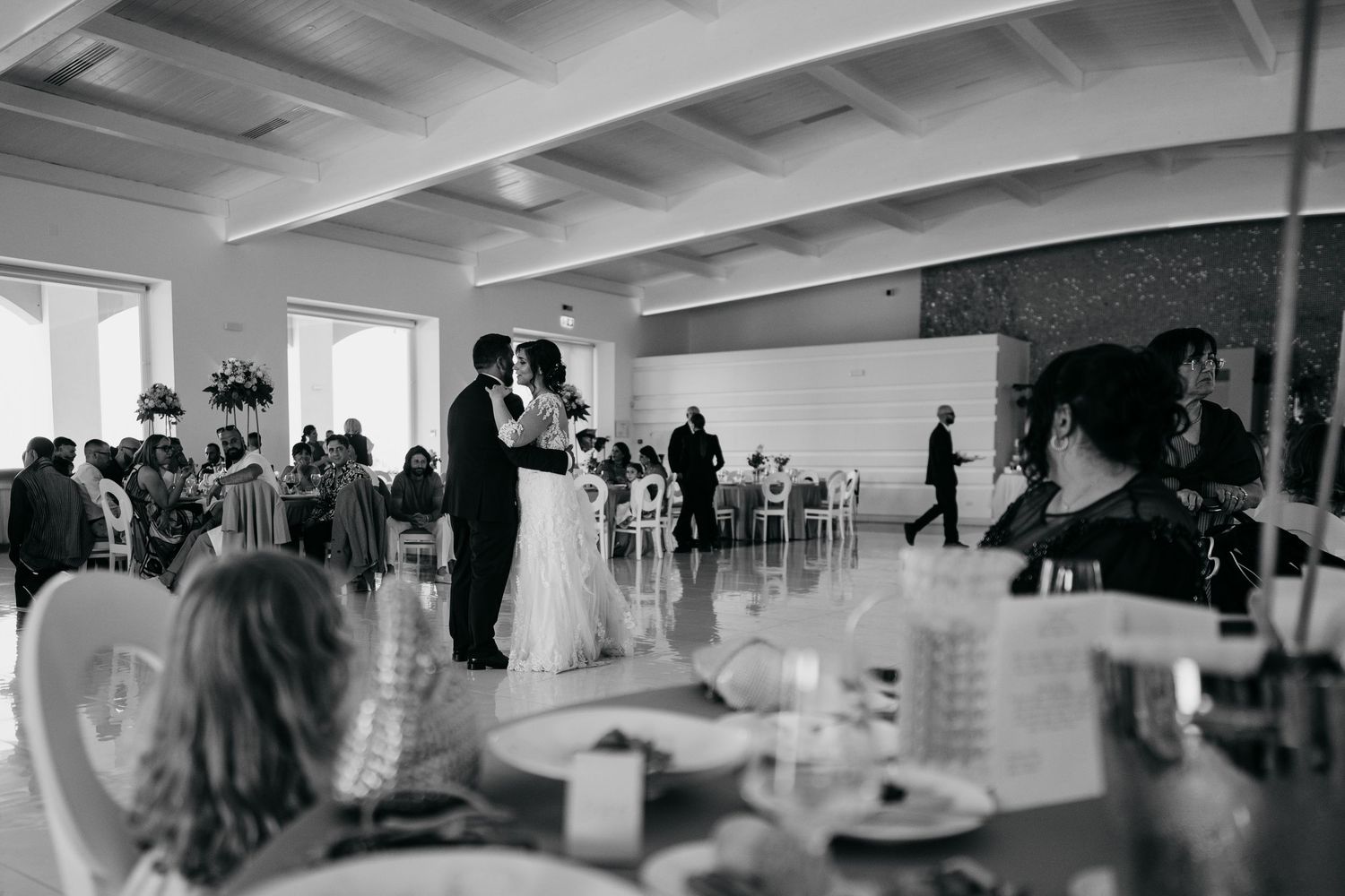 Black and white panoramic view of a wedding reception with guests mingling in a modern venue.