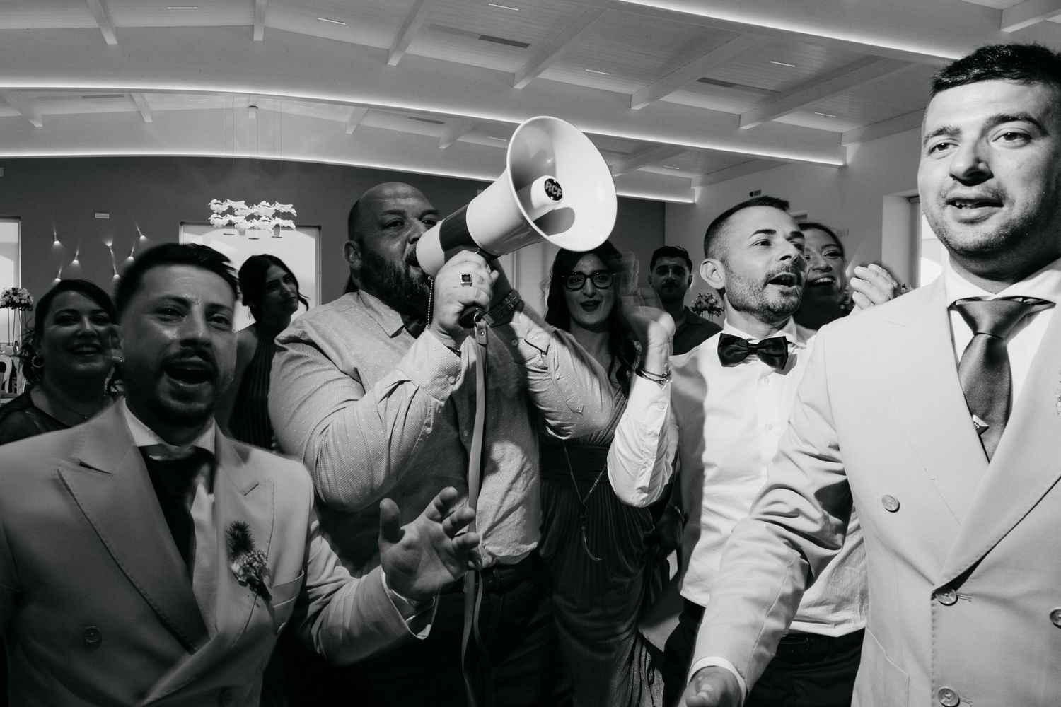 Wedding guests singing and celebrating with a megaphone at an indoor reception.