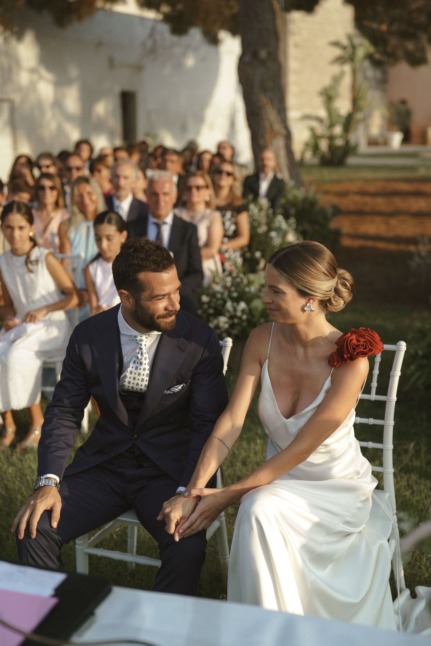 A joyful couple shares a tender moment during their outdoor wedding ceremony while guests look on.