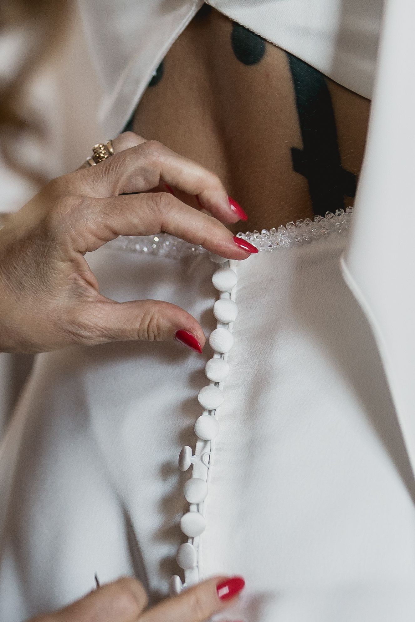 Close-up of hands with red nails fastening delicate buttons on a white wedding dress.