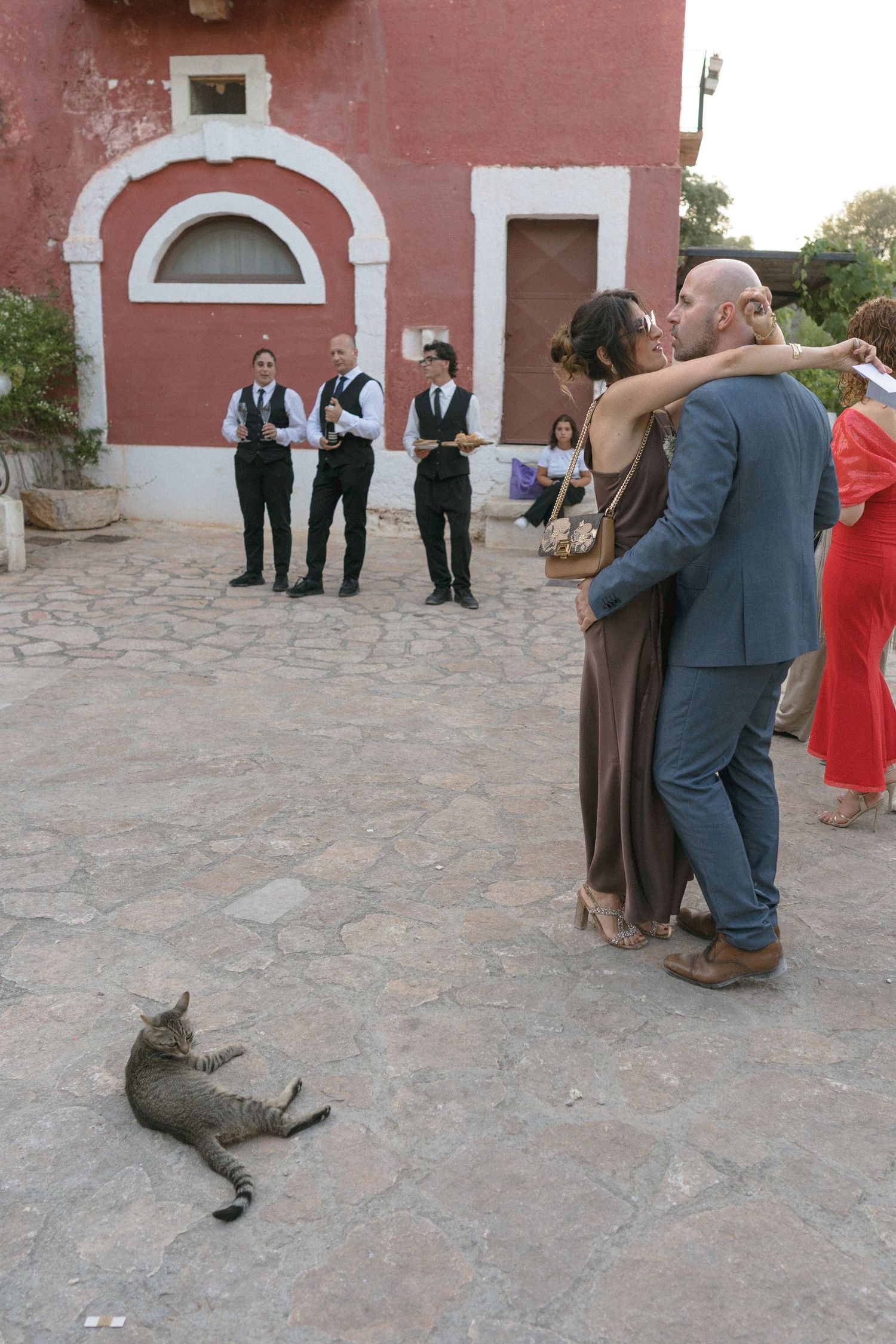 Wedding guests gather in a courtyard with pink stucco walls during an outdoor celebration.