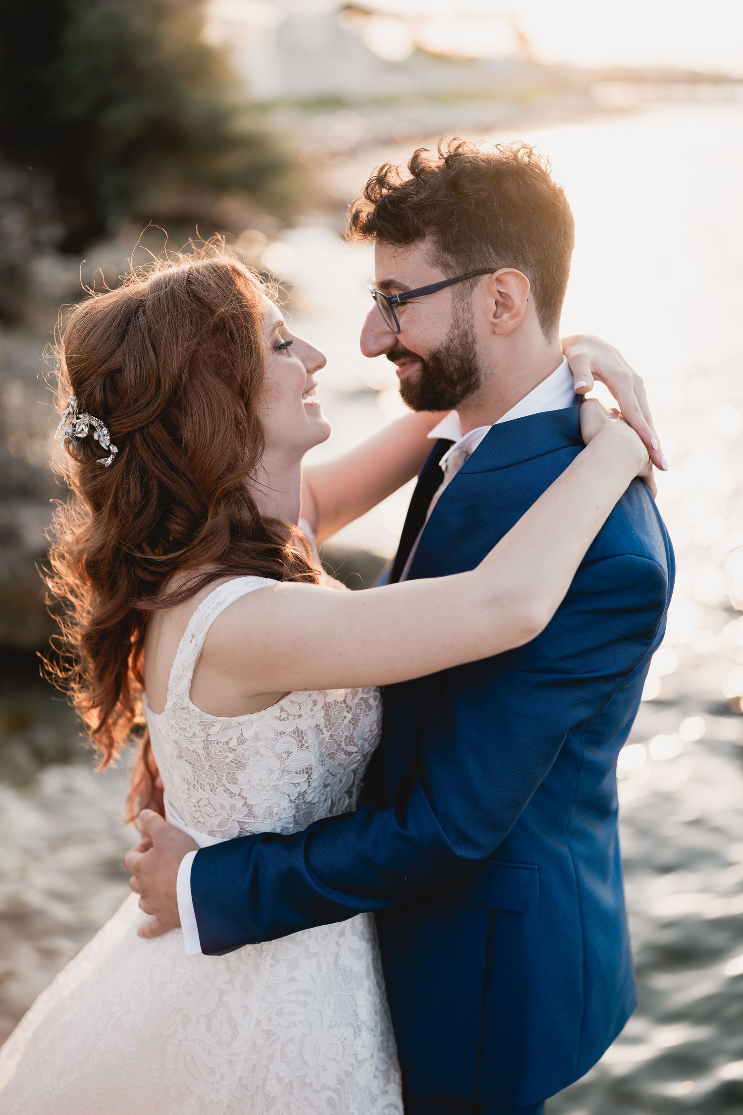 A romantic wedding photo of a couple embracing by the water during golden hour.