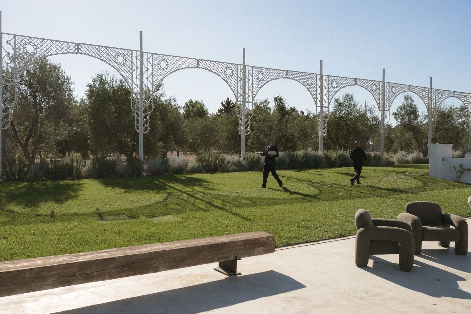 Elegant white arched garden trellis with manicured lawn at a sunny outdoor wedding venue.