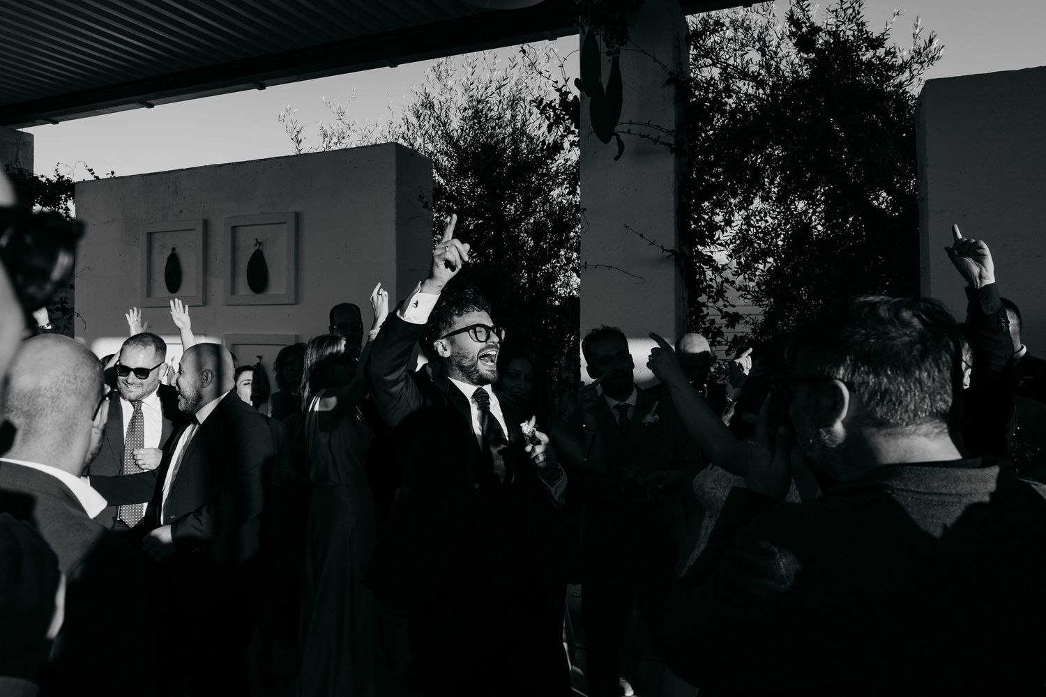 Wedding guests celebrate with hands raised at lively outdoor reception in black and white photo.