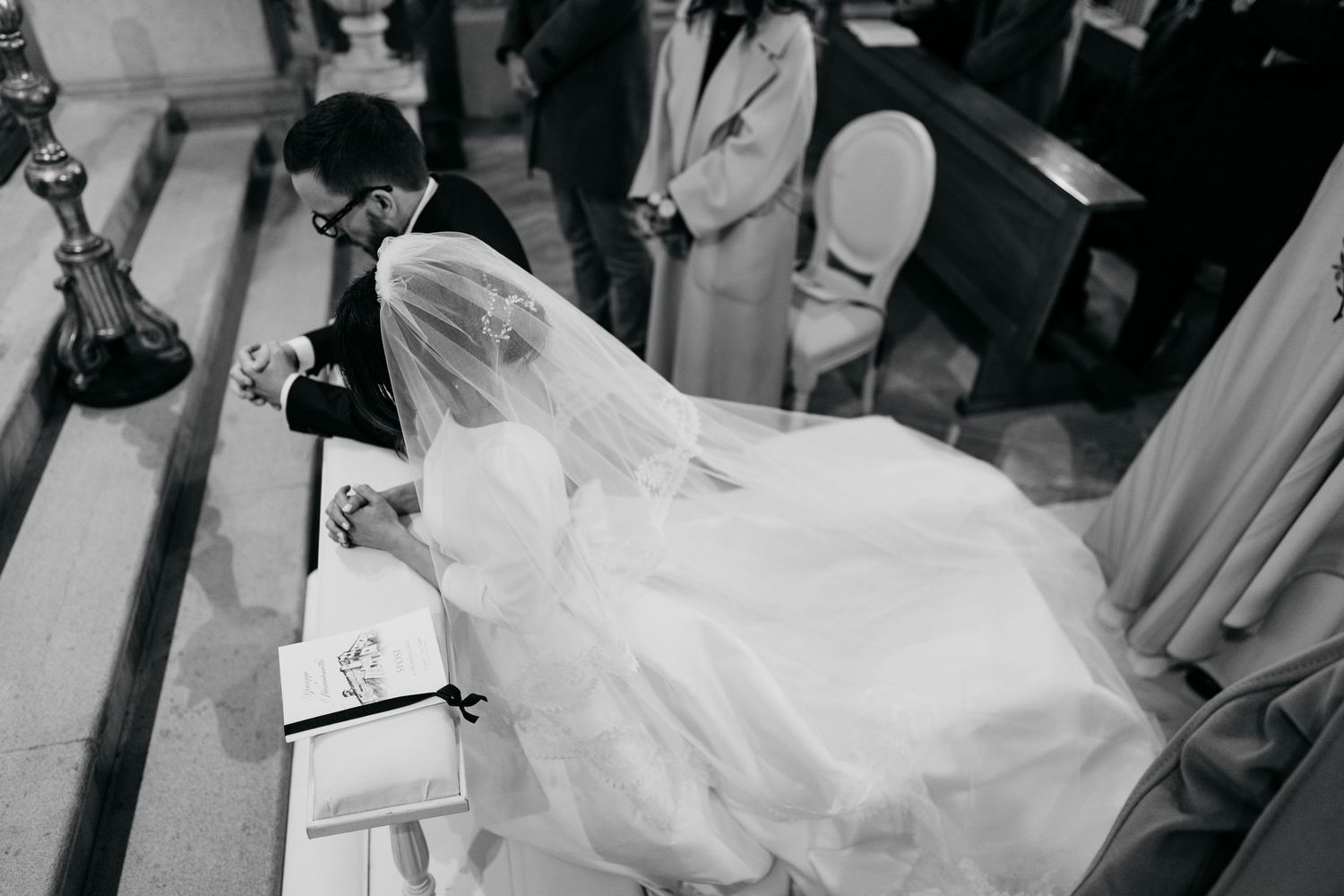 Black and white photo of a bride in a flowing veil and gown during a church wedding ceremony.