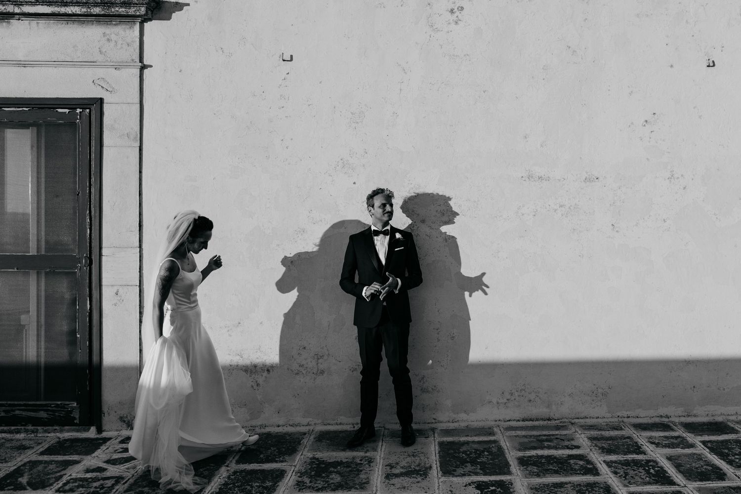 A black and white artistic photo of two people casting dramatic shadows on a white wall.