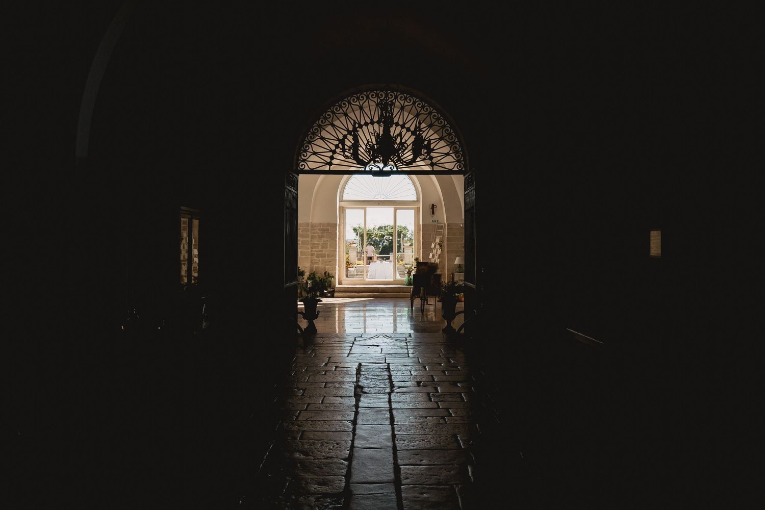 Dark arched hallway leading to illuminated doorway in historic stone building.