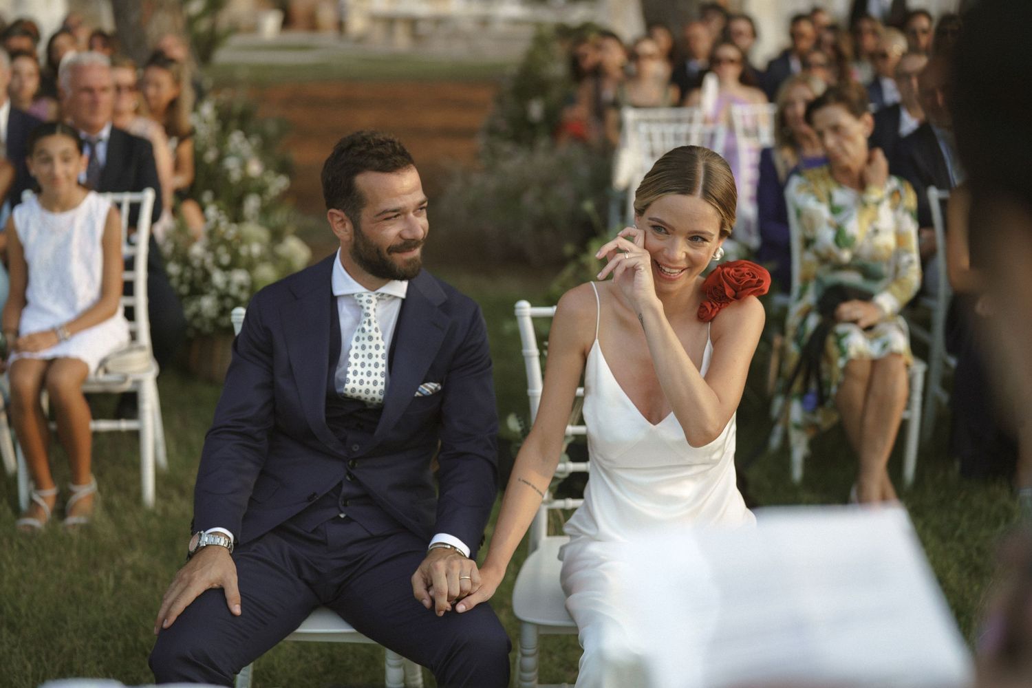 An emotional moment during an outdoor wedding ceremony with guests seated in the background.