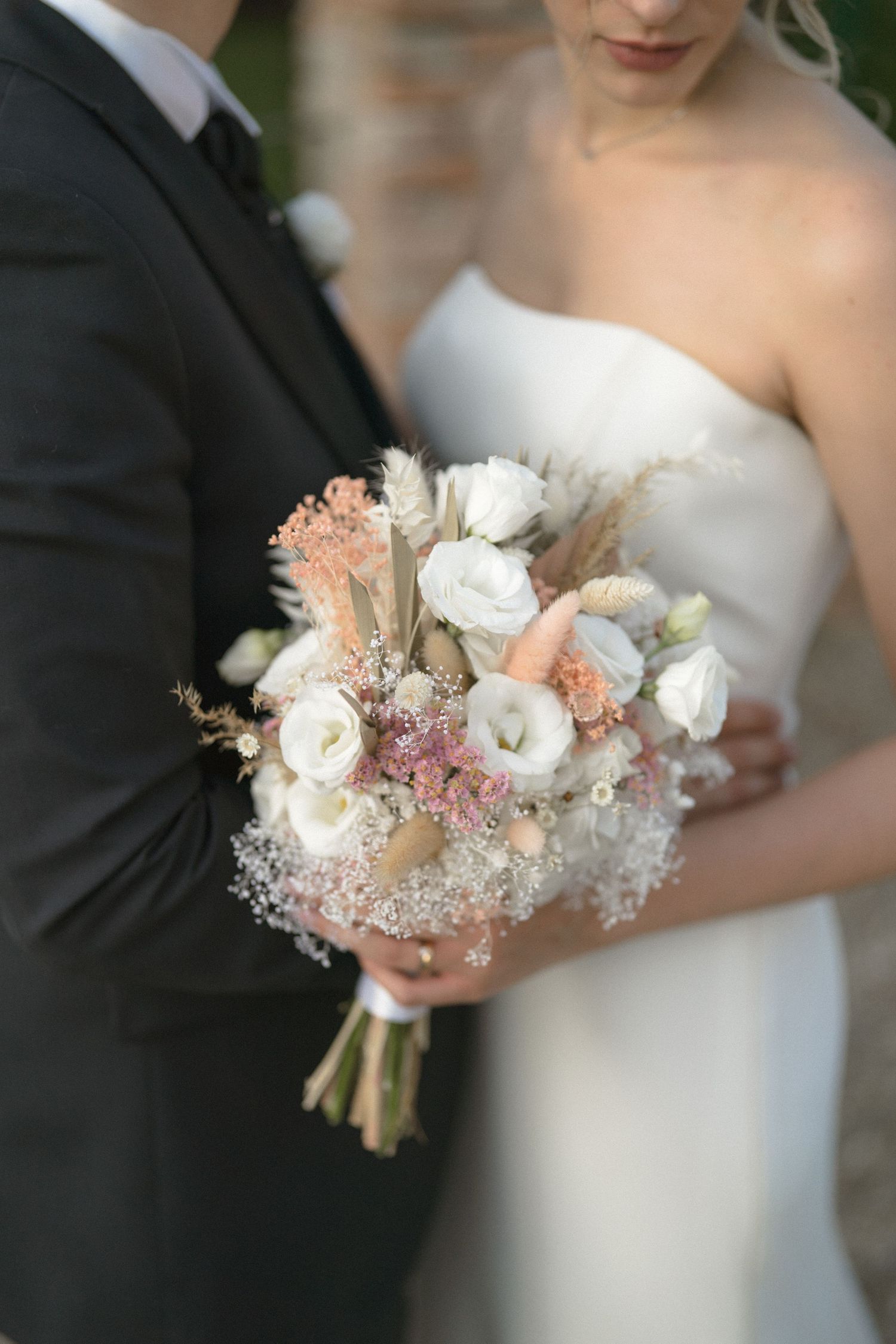 Delicate wedding bouquet featuring white and peach flowers with dried elements.