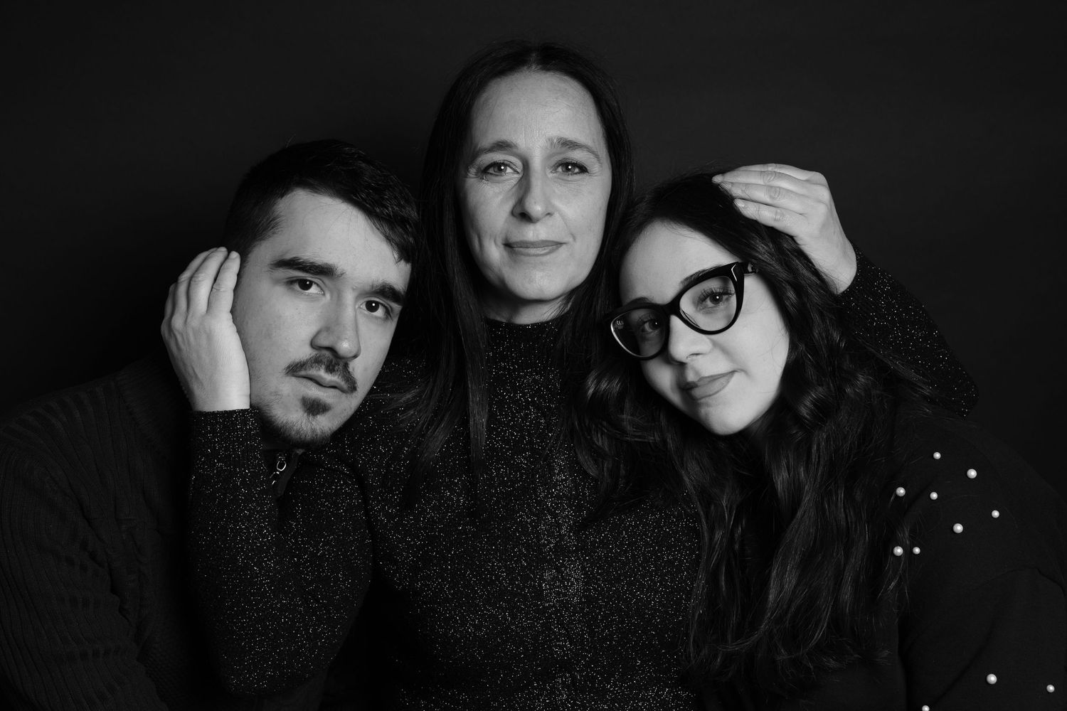 Ritratto in bianco e nero di tre persone che indossano maglioni scuri su uno sfondo scuro.