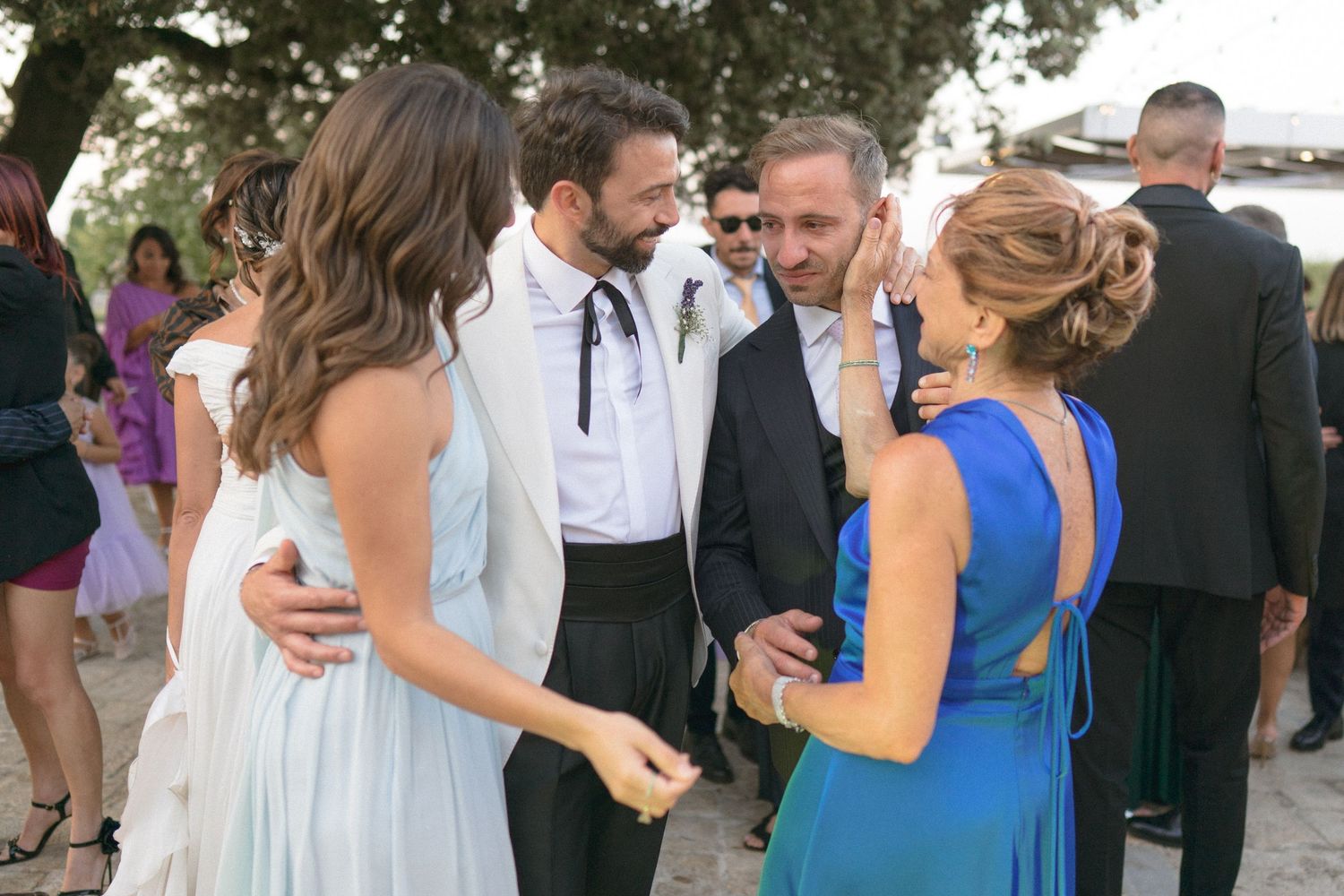 Wedding guests in formal attire share an animated conversation during an outdoor reception.