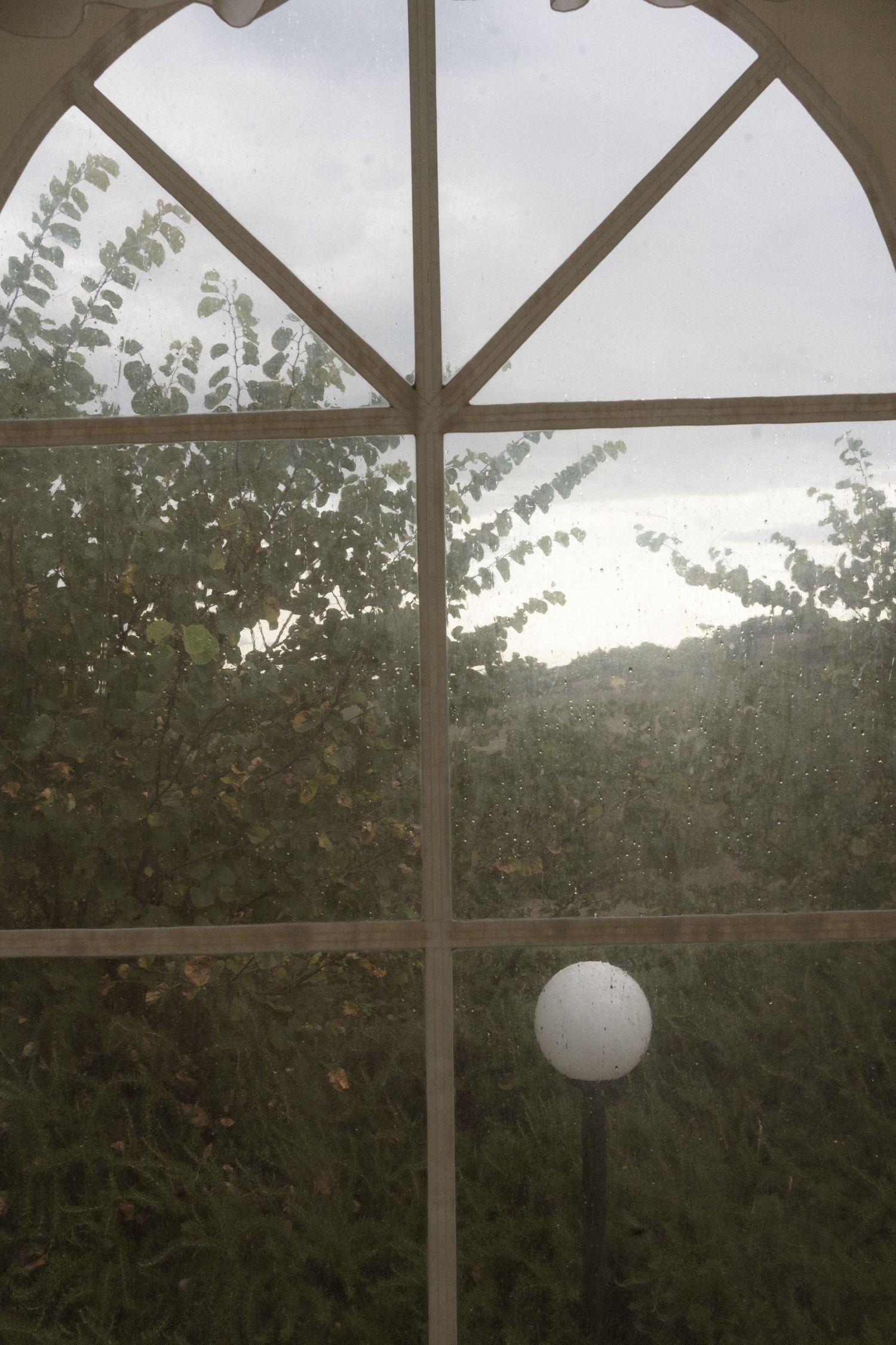 White globe pendant light hangs from wooden beams in a covered outdoor space.