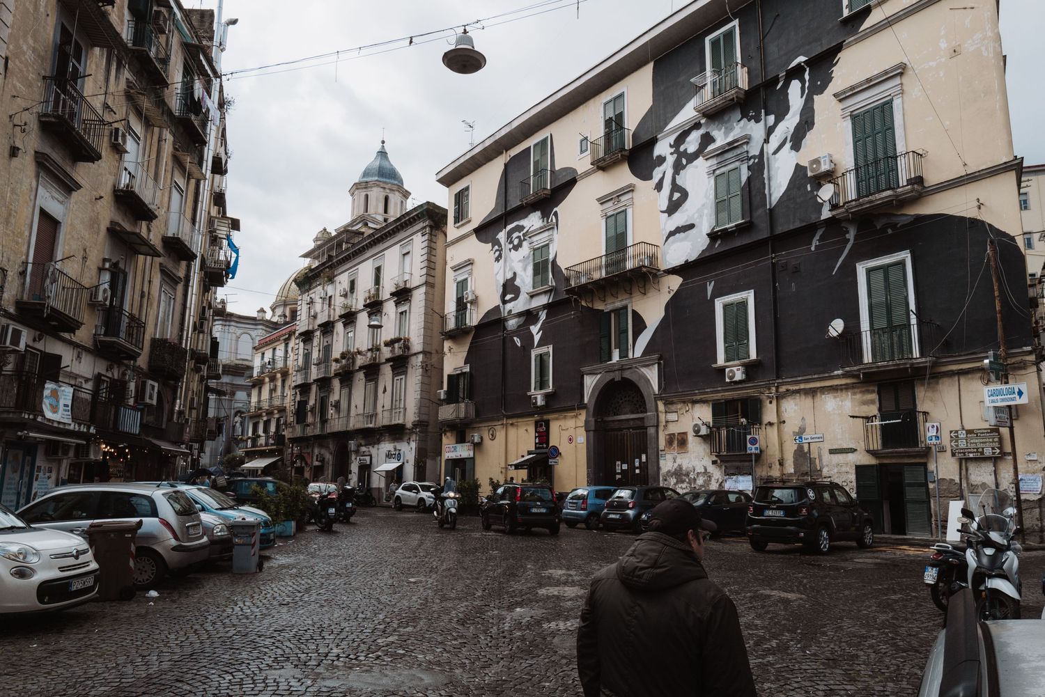 A narrow cobblestone street lined with historic buildings and parked vehicles in an Italian neighborhood.