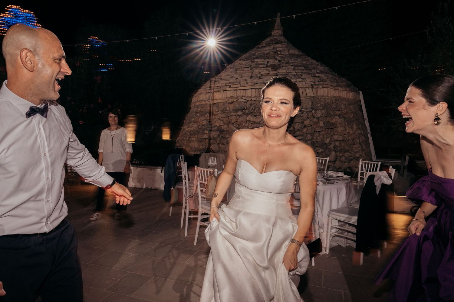 Wedding guests dance and celebrate at an evening outdoor reception with string lights.