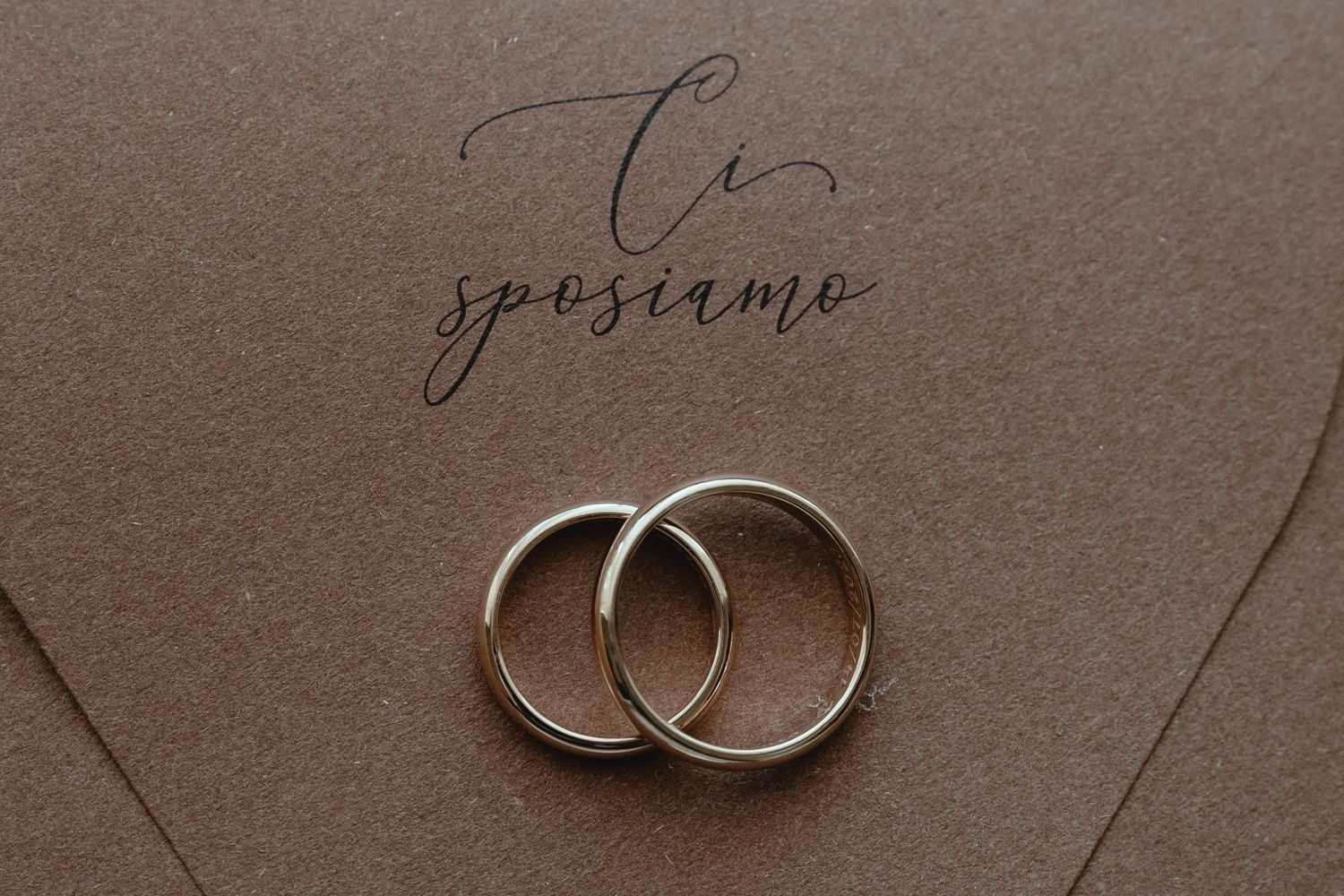 Two wedding rings placed on a brown envelope with elegant cursive text.