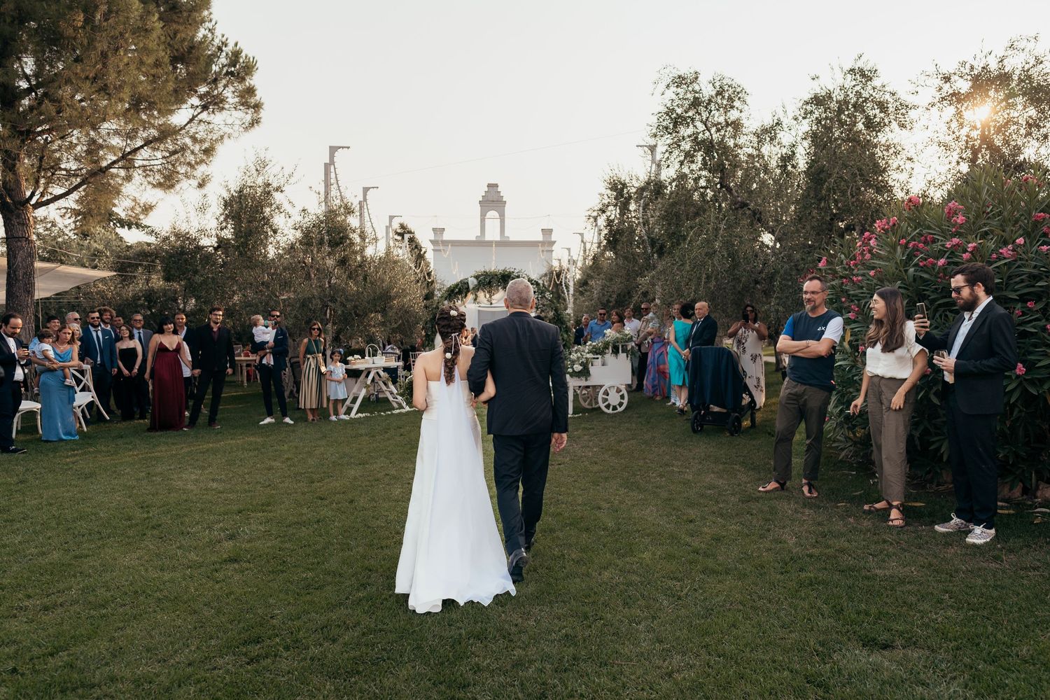 Wedding ceremony on grass lawn with guests gathered around at sunset.