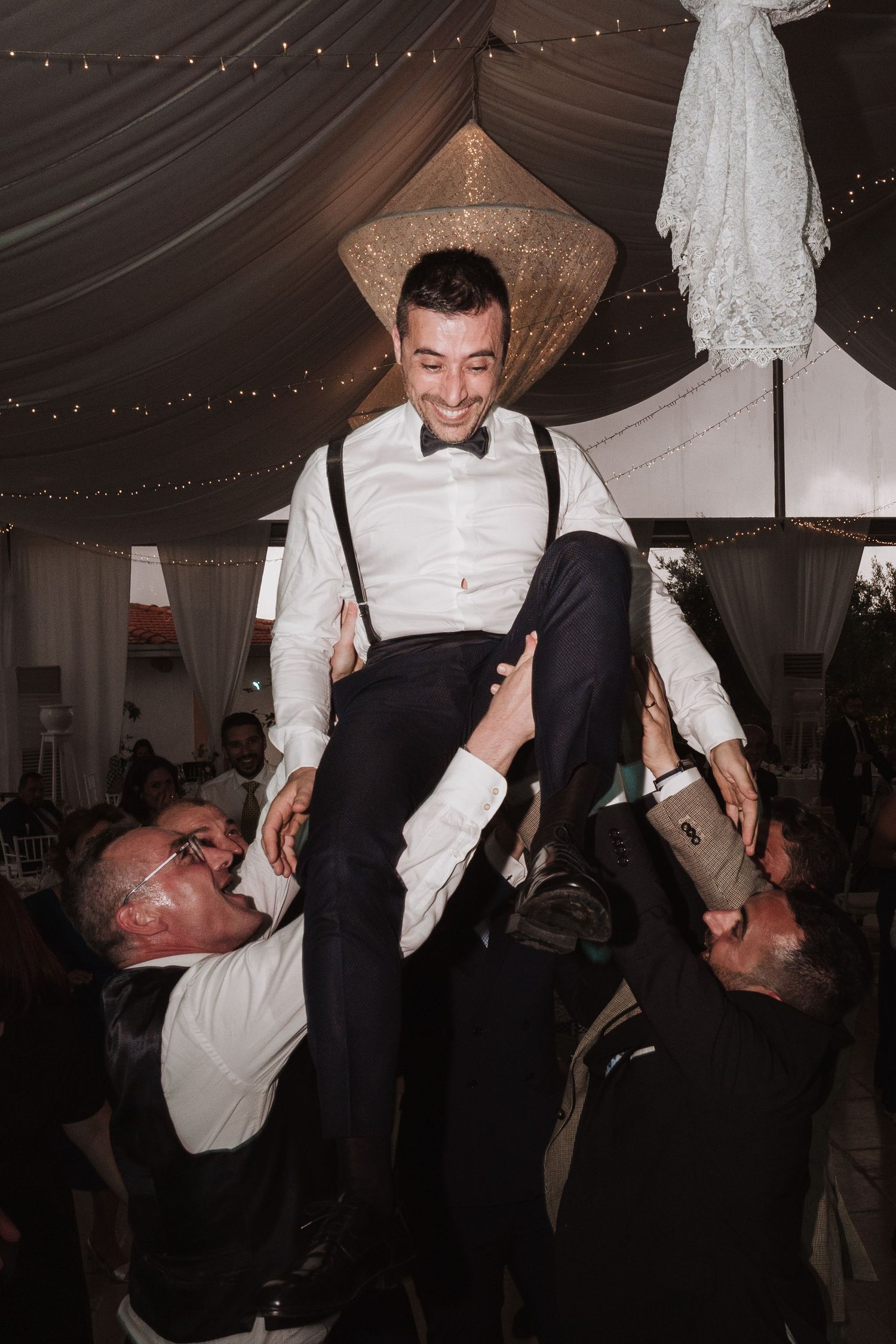 Celebration at a wedding reception with guests lifting someone up in the air.