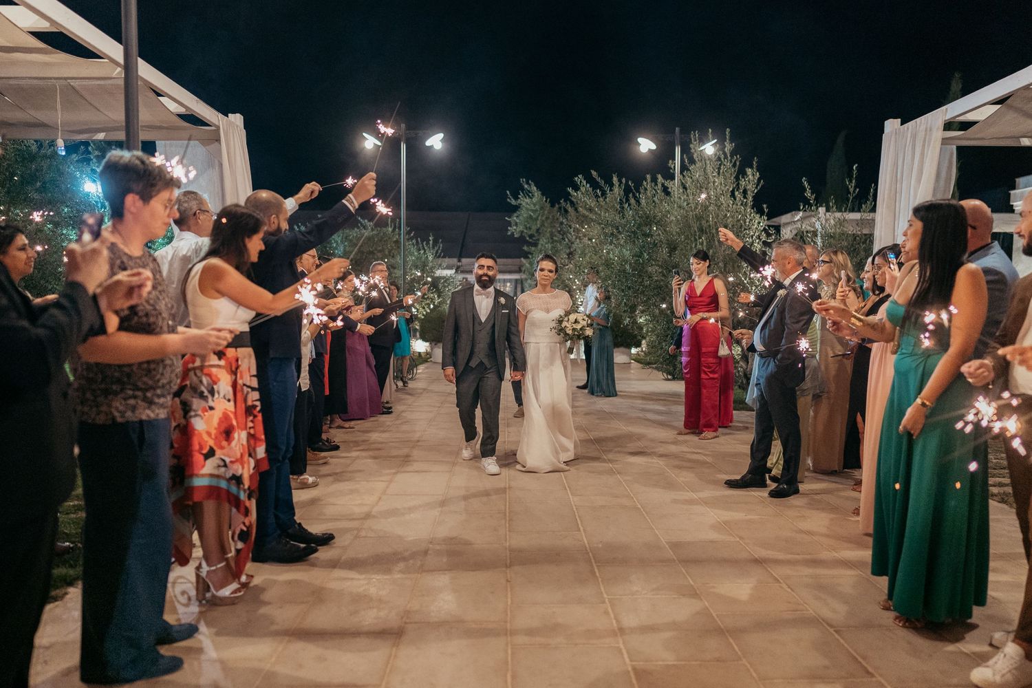 Wedding guests form an illuminated pathway outdoors for the couple's grand exit.
