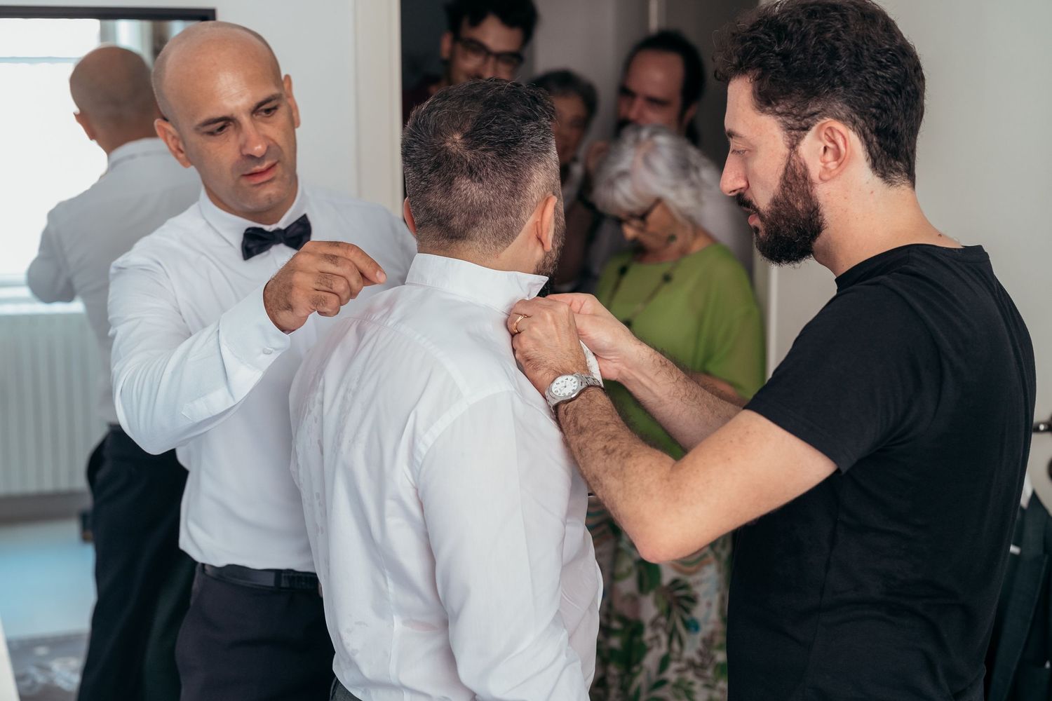 Wedding preparations showing formal attire adjustments in a bright room.
