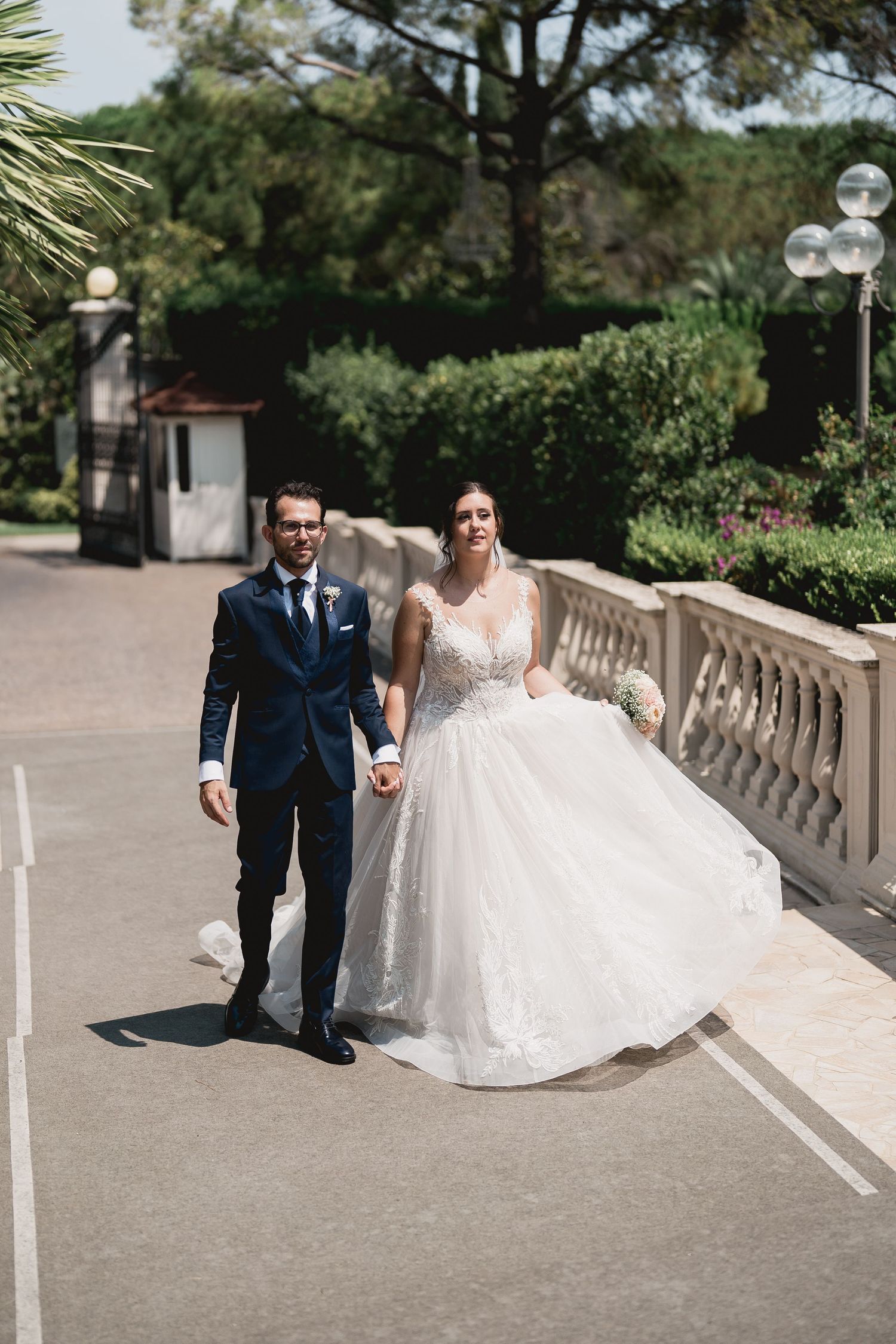 Newlyweds walking together on a sunny paved pathway outdoors.