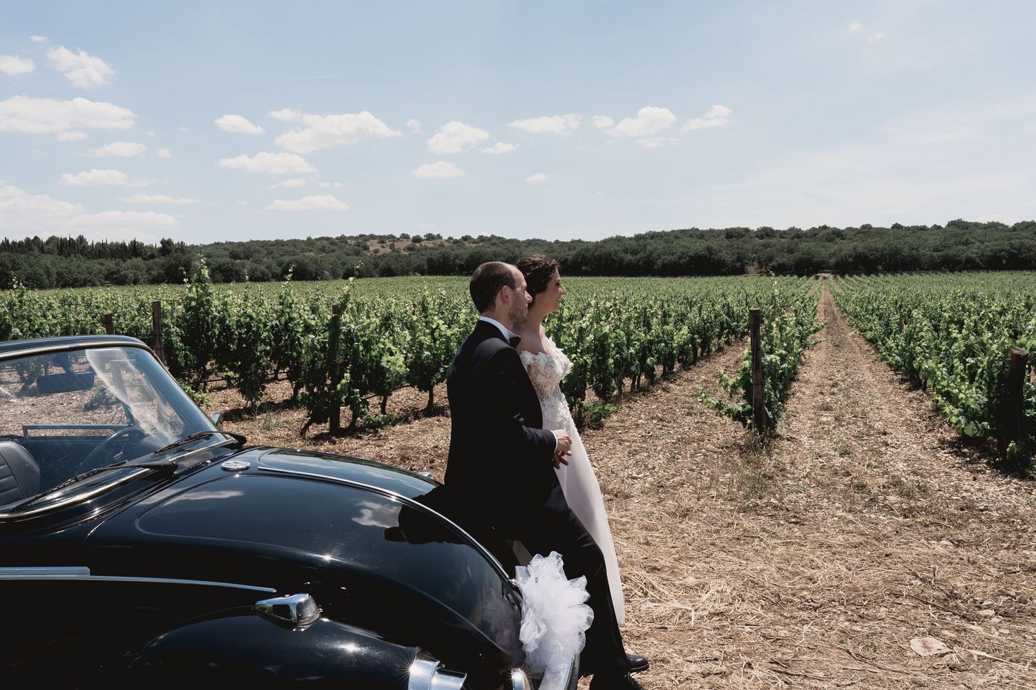 A classic car adds vintage charm to wedding photos taken in a scenic vineyard setting.