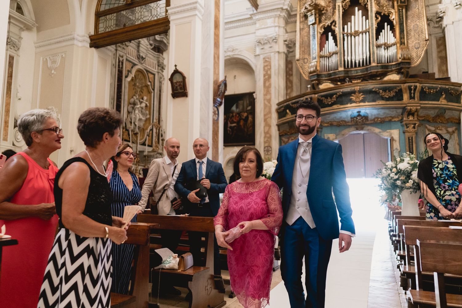 Wedding ceremony guests observe couple walking down church aisle with ornate organ pipes visible.