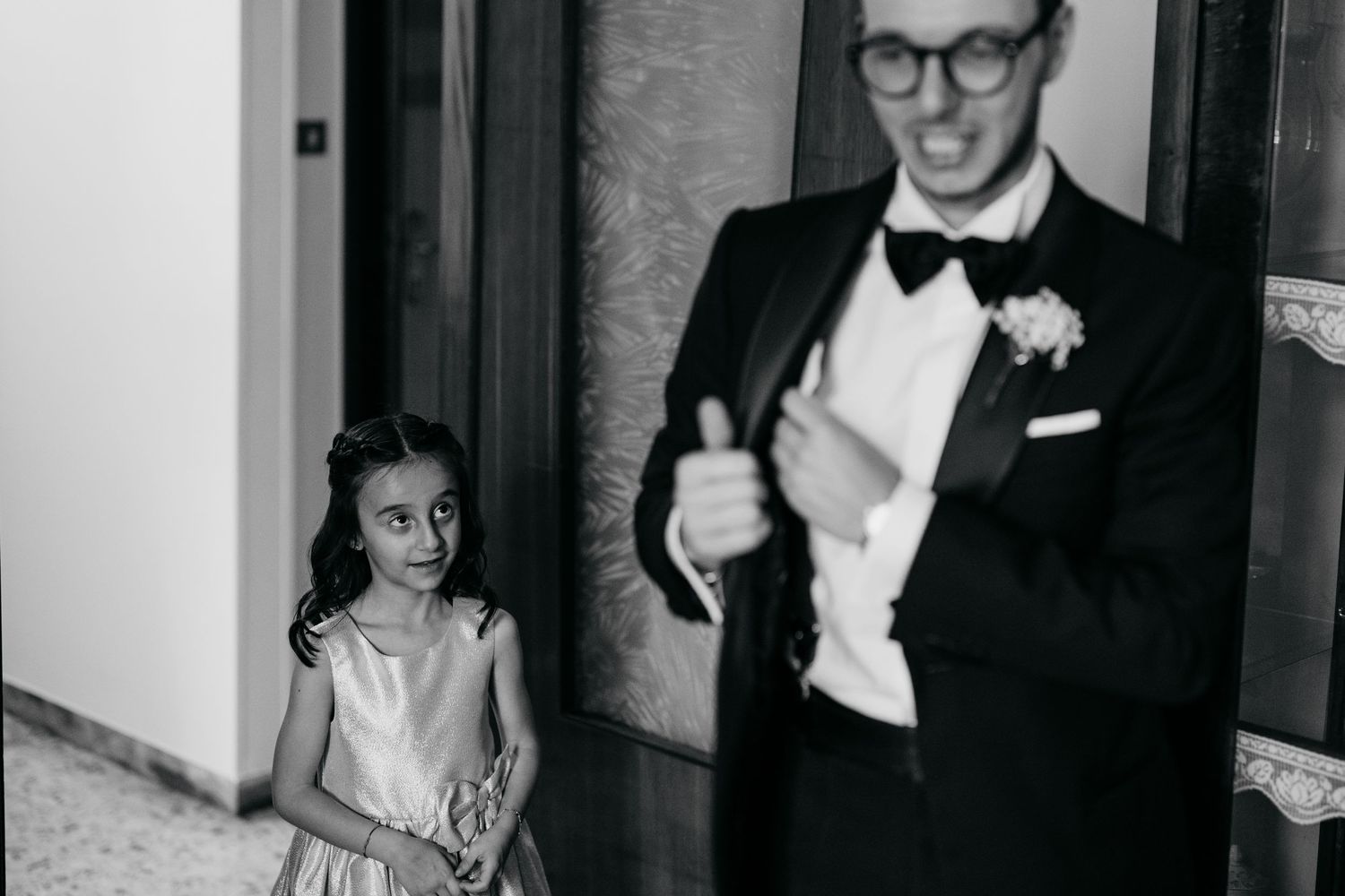 Black and white candid moment of formal wedding attire in a hallway.