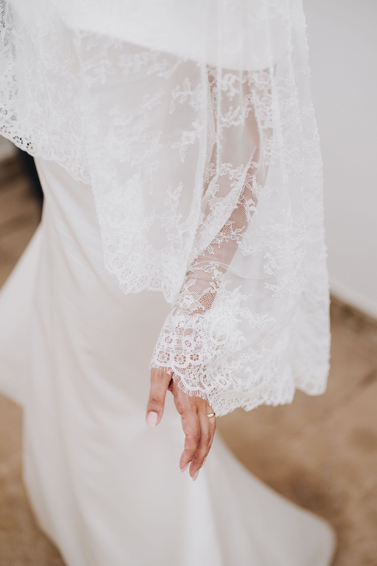 Delicate white lace sleeve detail of a wedding dress with intricate floral patterns.